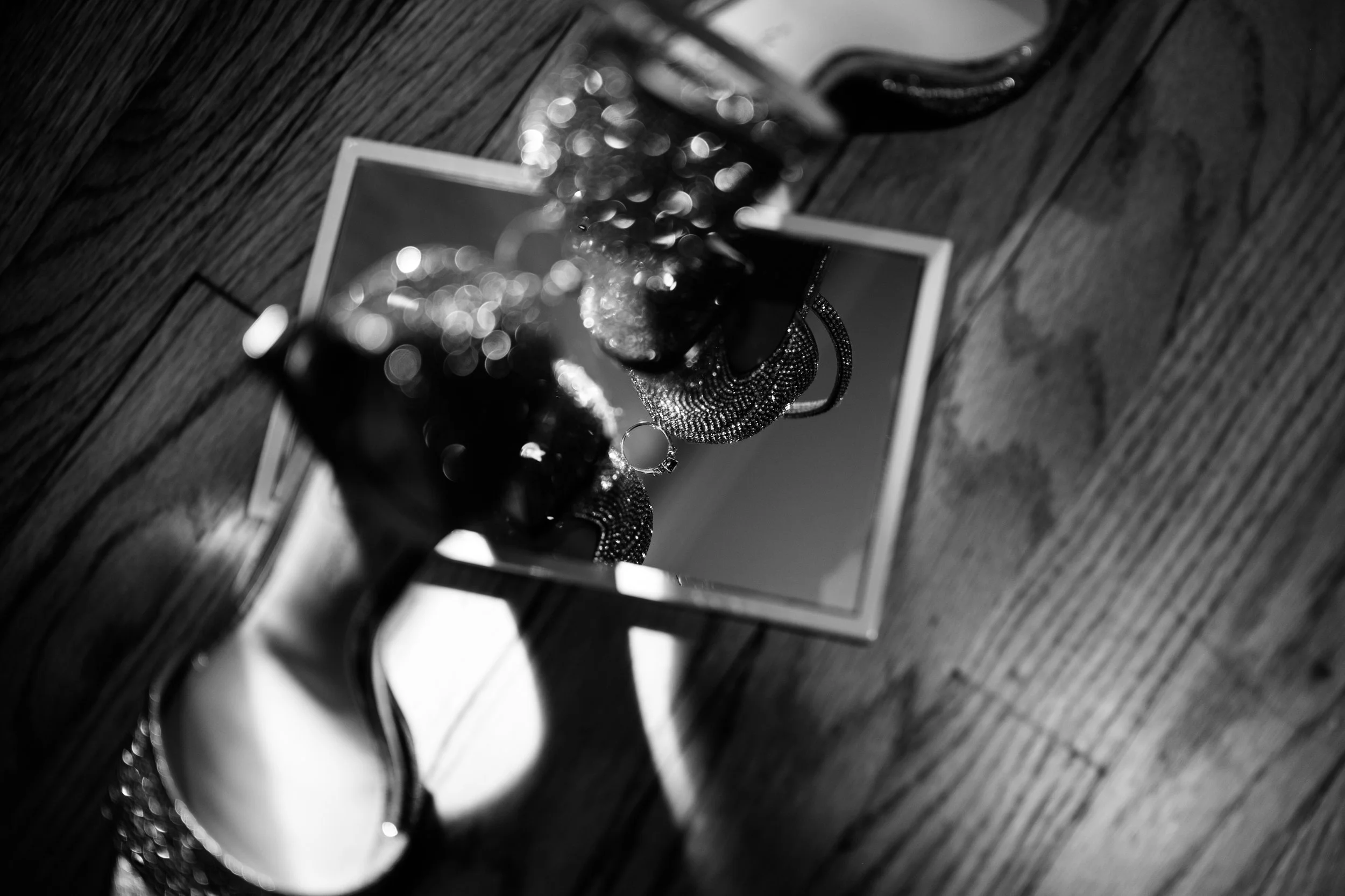 A reflective surface showing jewelry, including a ring, necklaces, and earrings, resting on a wooden floor.