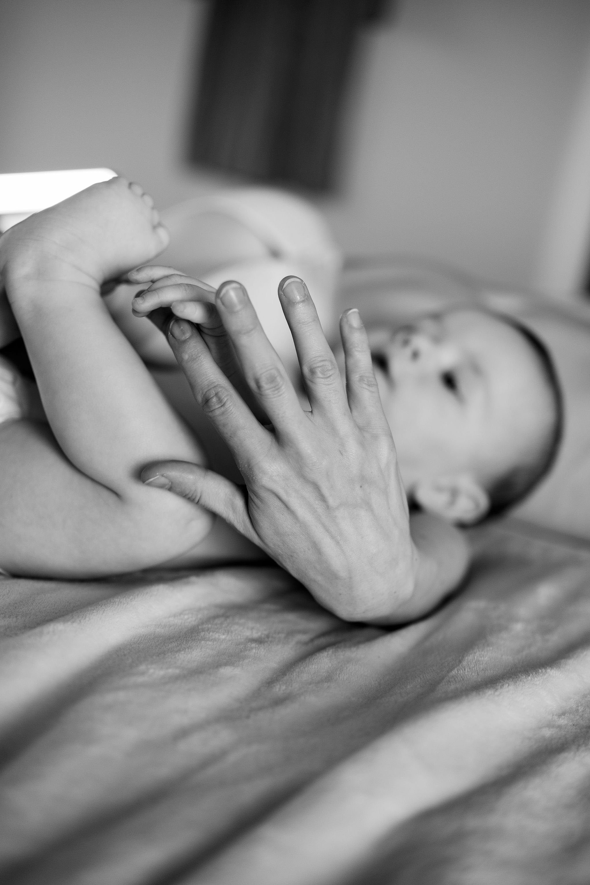 A child lying on a bed with an adult's hand gently holding their arm, in black and white.