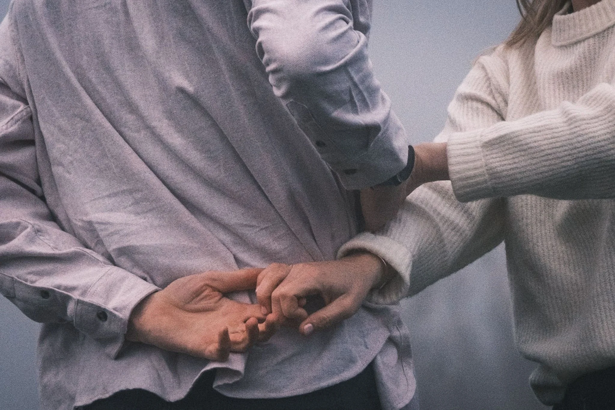 Two people gently holding hands, with one person wearing a gray jacket and the other wearing a beige sweater.