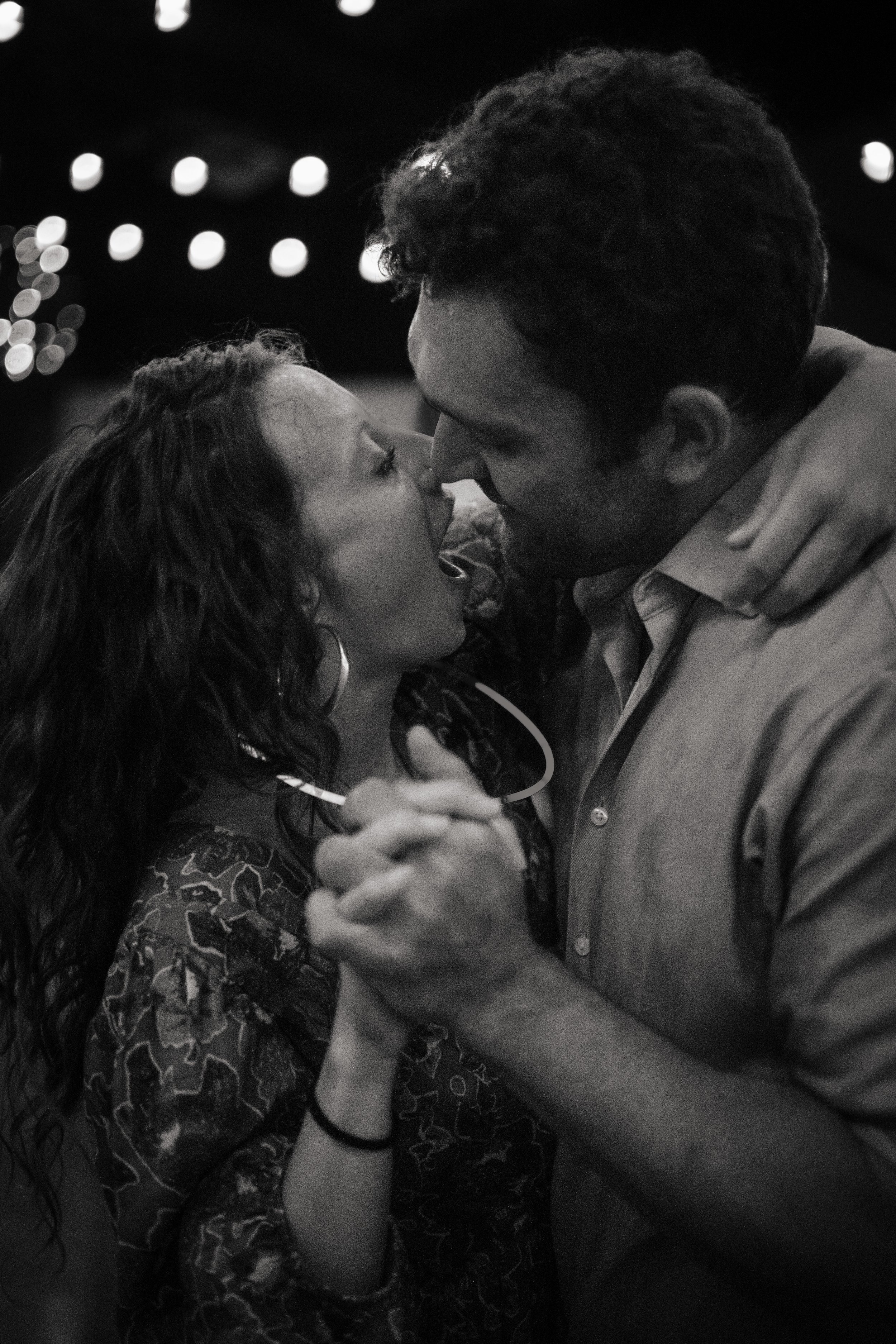 A black-and-white photo of a couple dancing closely, with the woman leaning back, hair falling to one side, and the man holding her as they gaze into each other's eyes.