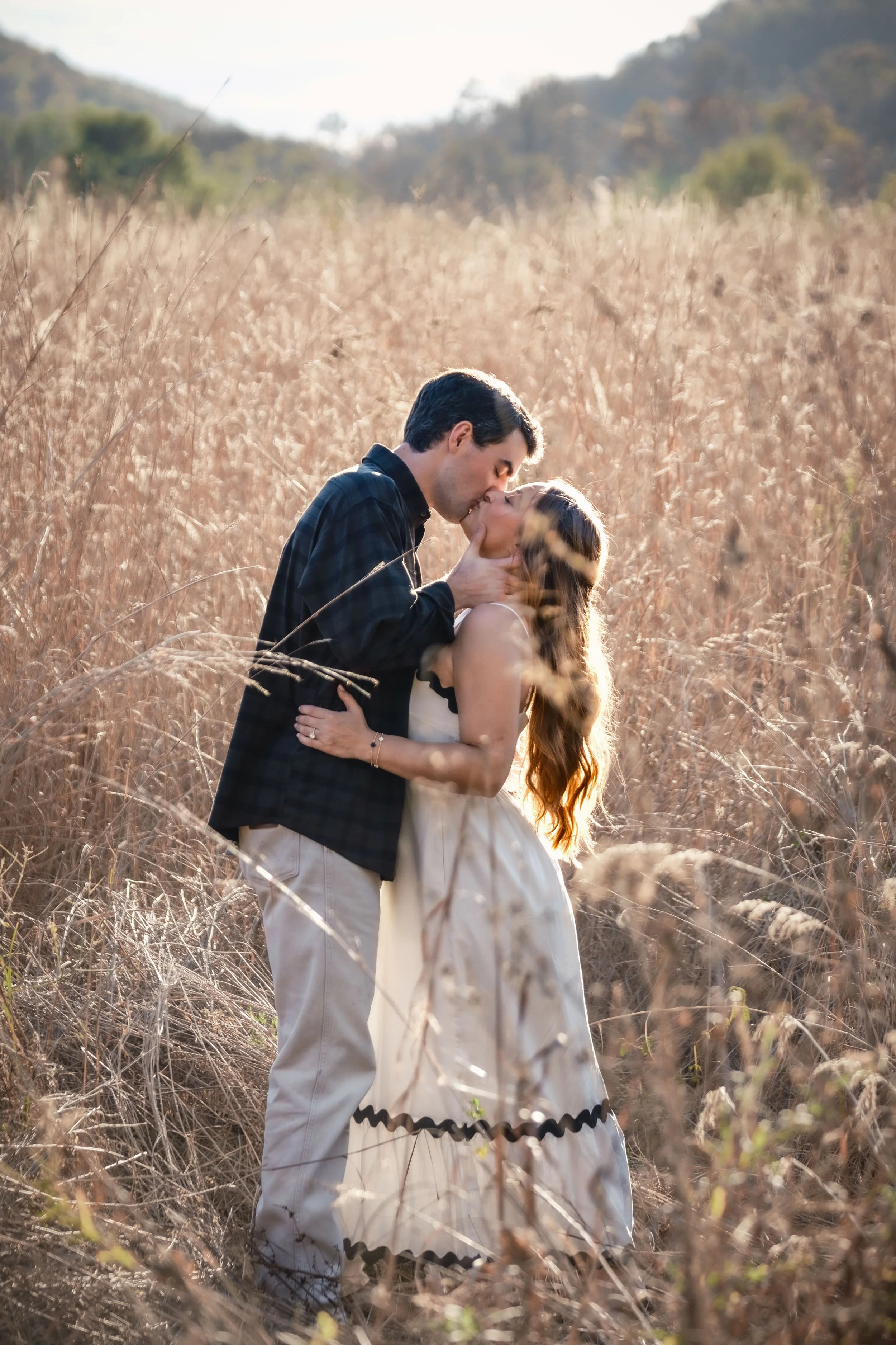 A couple kissing in a field of tall, dry grass during sunset.