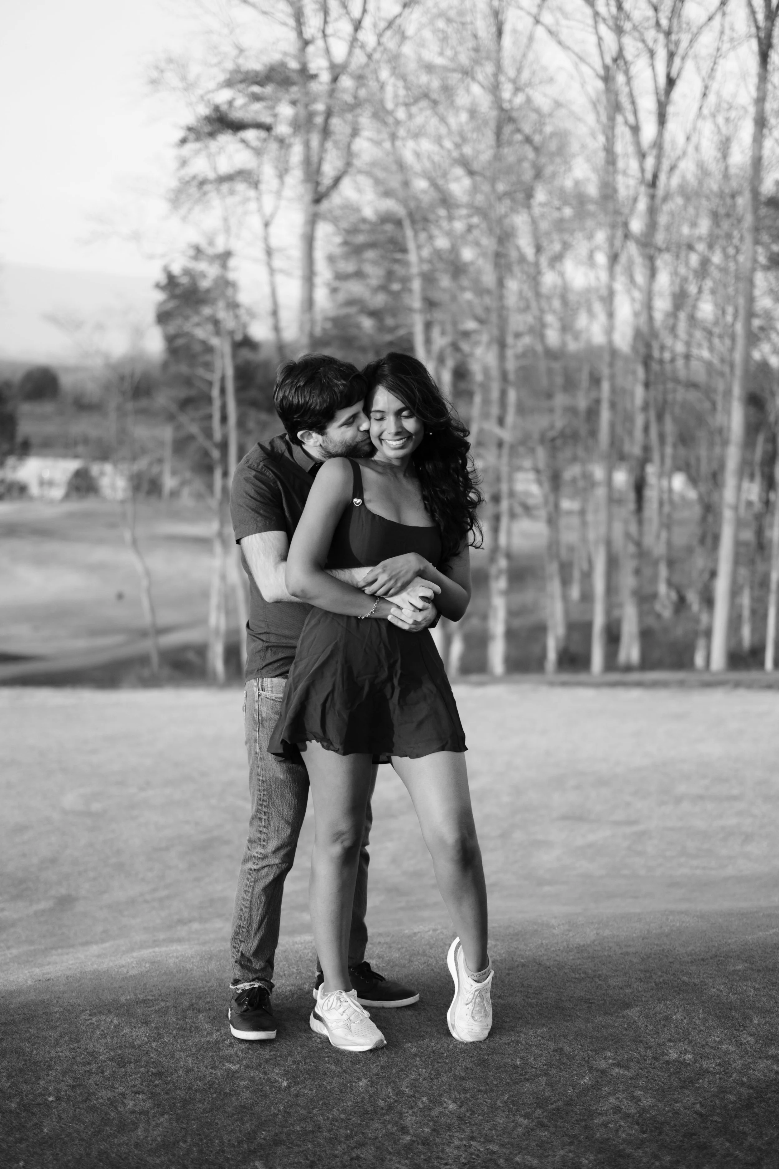 A couple embracing and smiling outdoors on a golf course, in black and white.