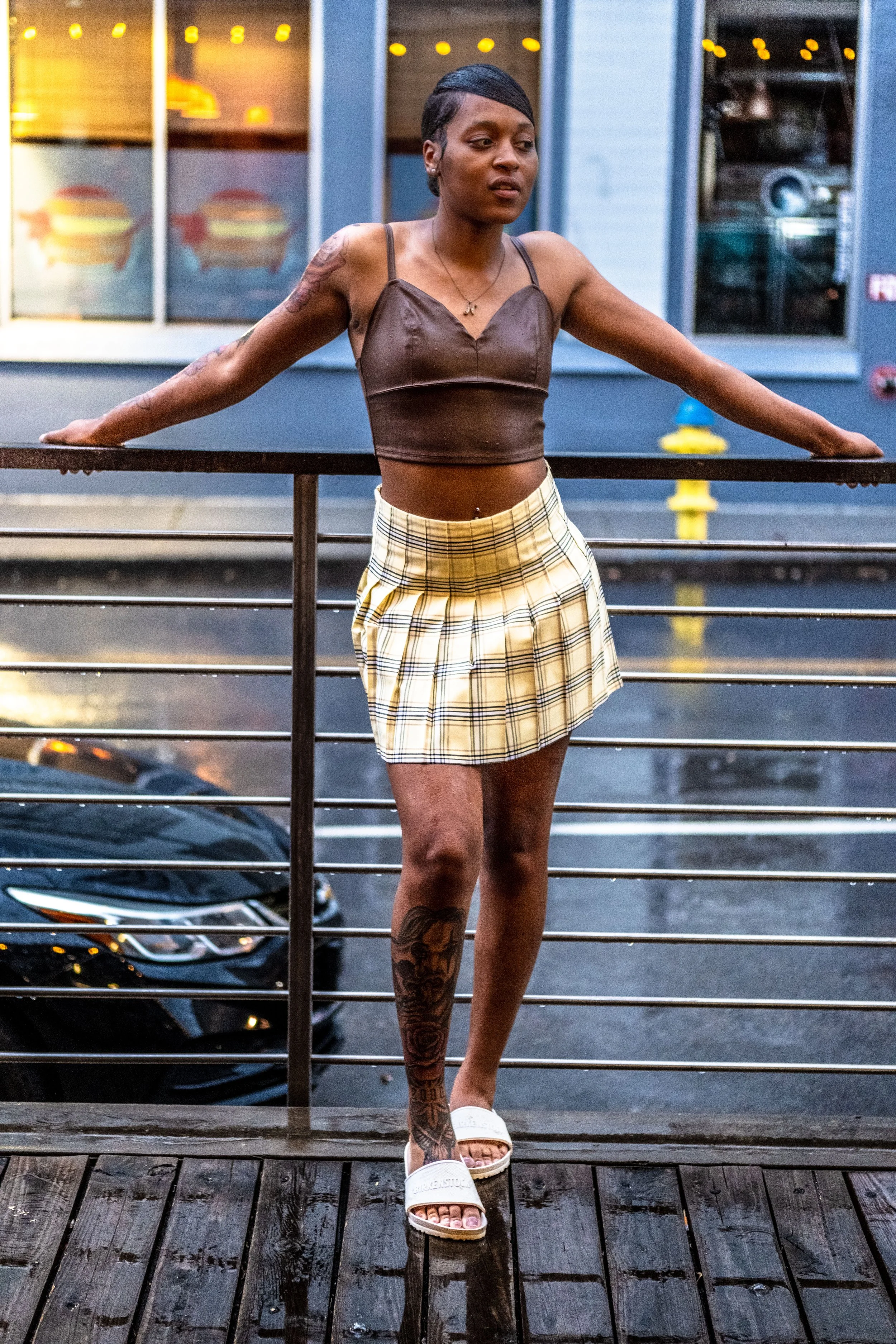 A woman standing on a wooden deck, holding onto a metal railing, with a restaurant exterior and a parked car in the background.
