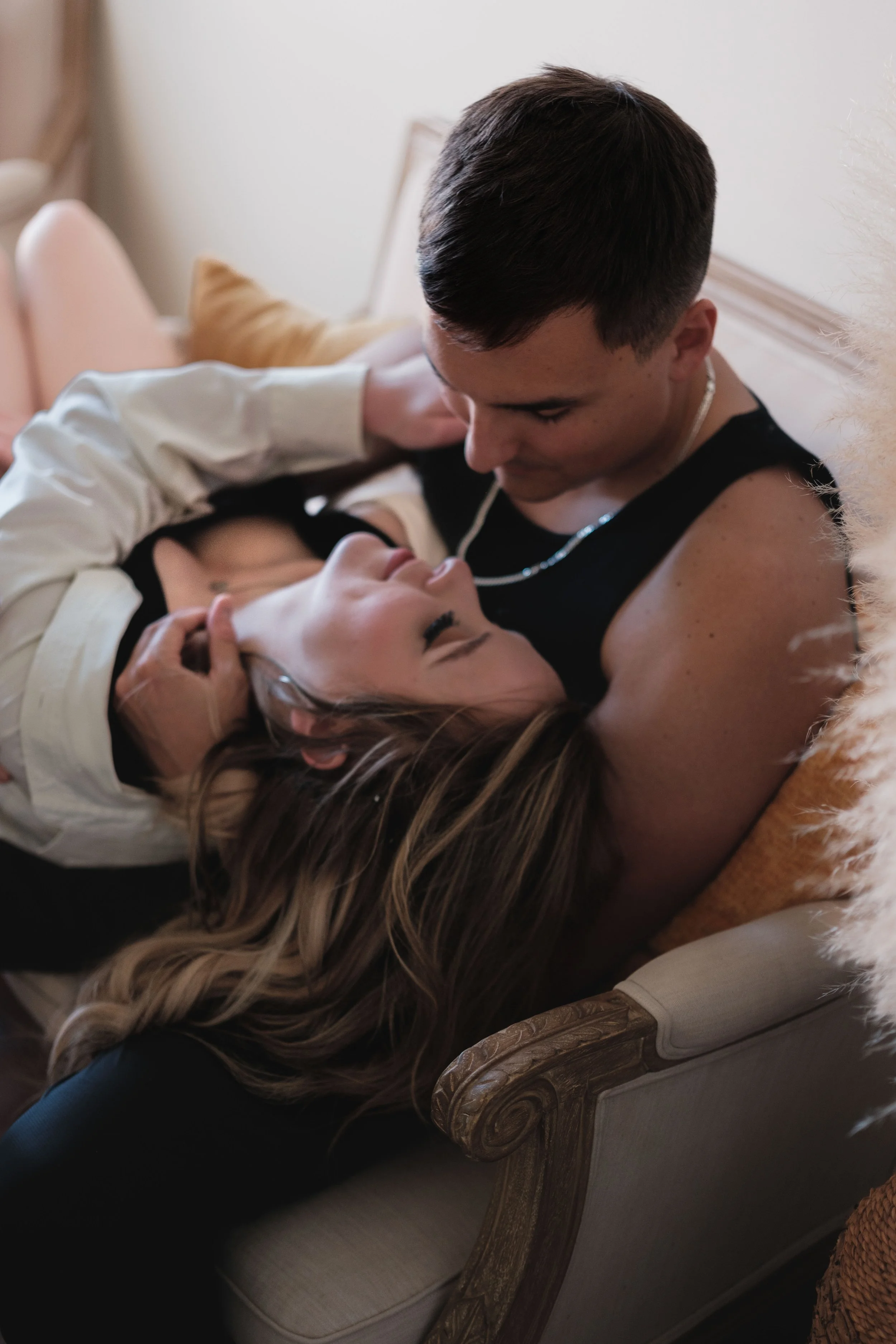 A couple lying on a sofa, embracing each other, looking at each other lovingly, with the woman resting her head on the man's lap and the man holding her face.