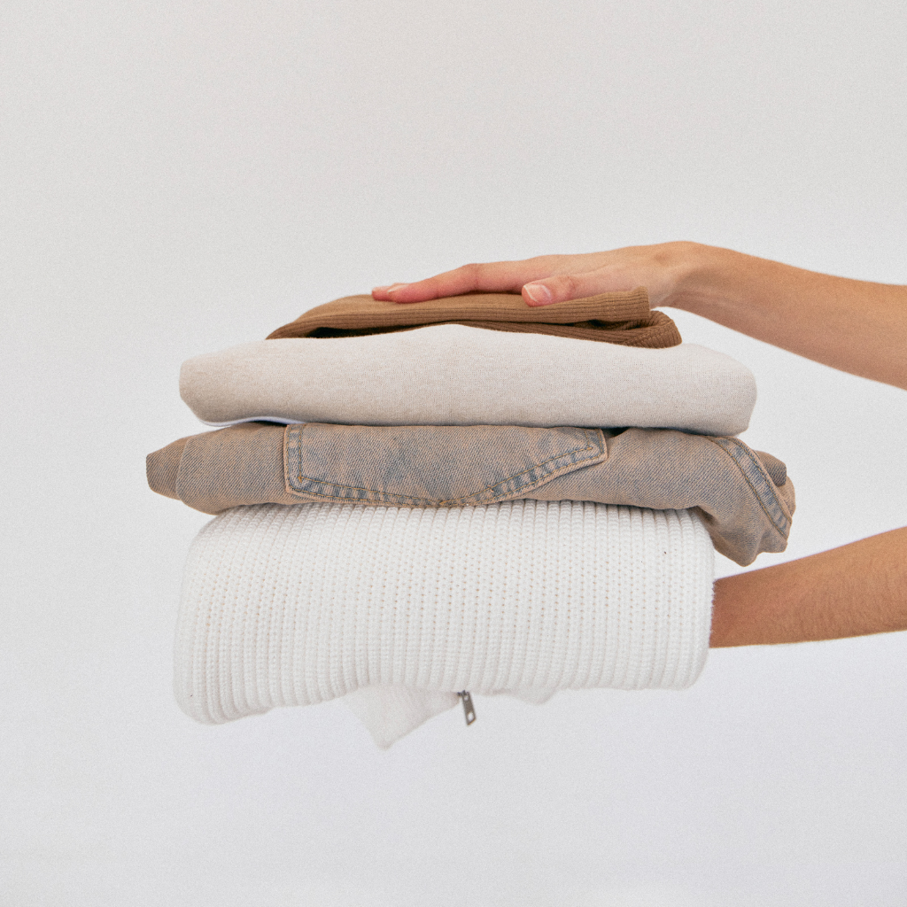 Person holding a neatly and freshly laundered folded stack of clothes against a plain white background.