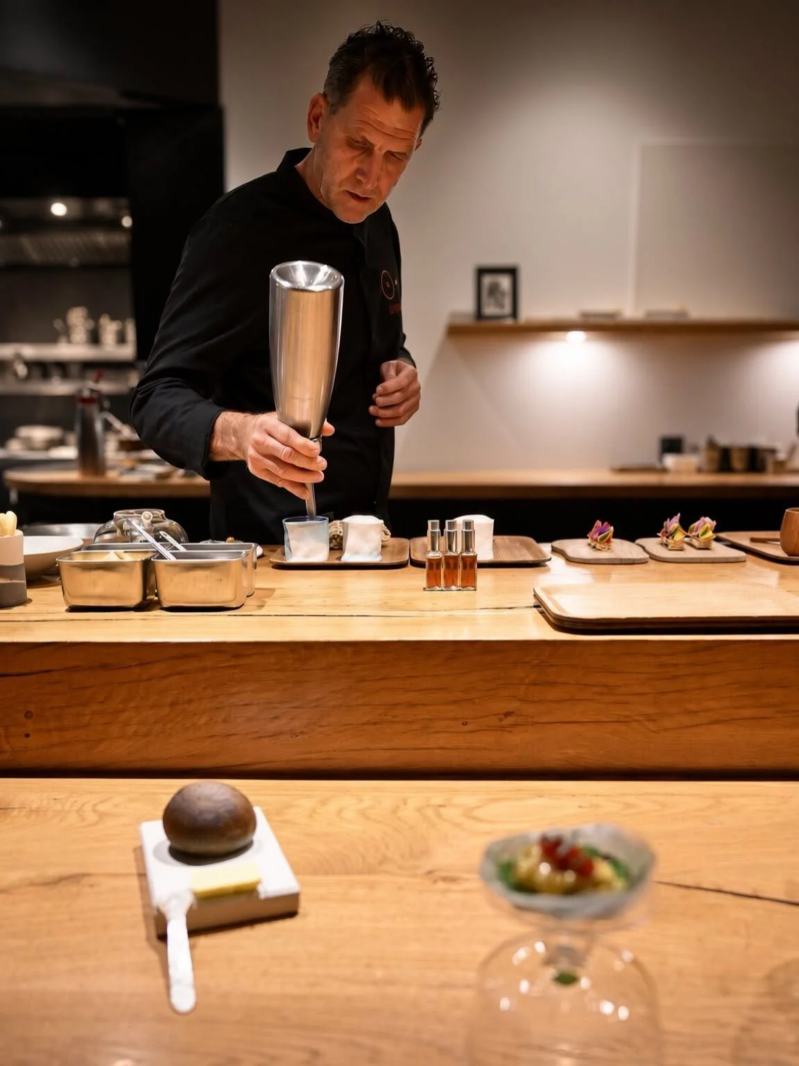 Cuisinier en tenue noire préparant une séquence derrière le comptoir face aux convives
