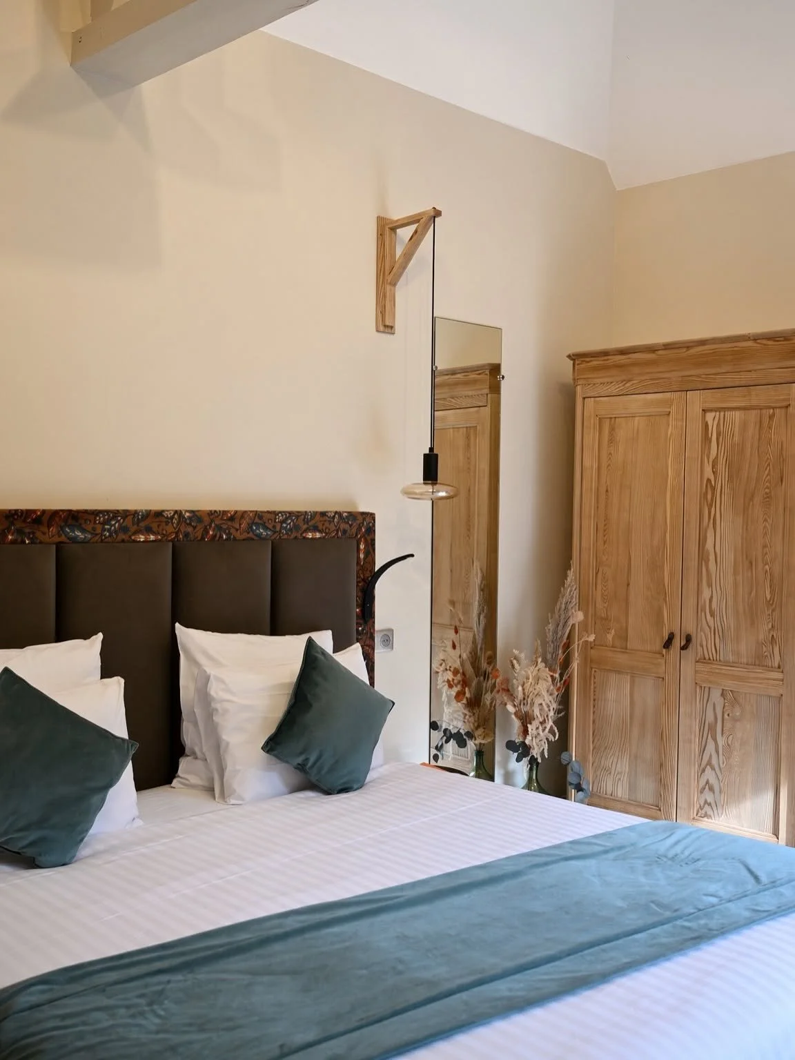 Chambre lumineuse avec tête de lit sombre, coussins bleu canard et armoire en bois