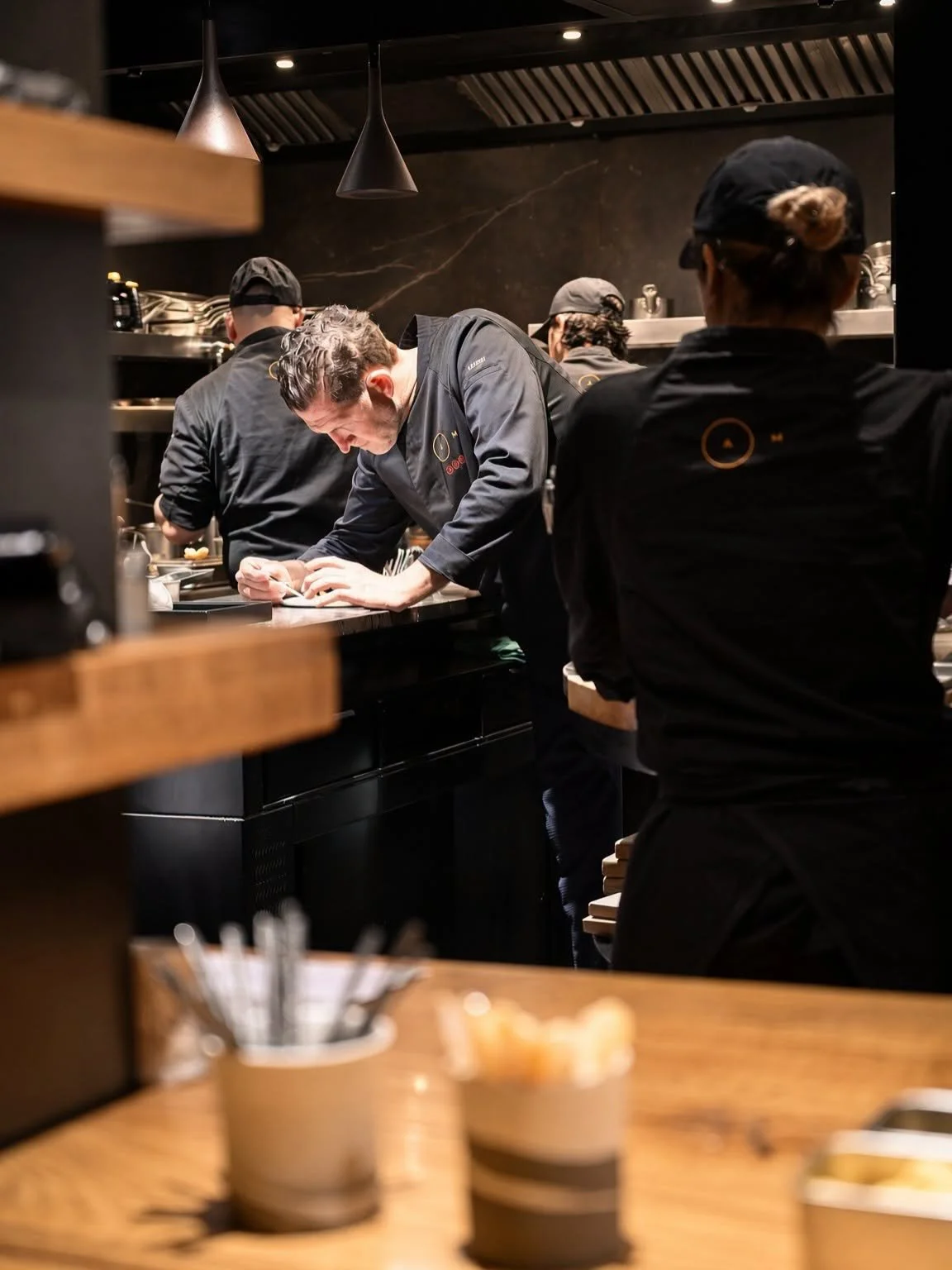 La brigade d'AM concentrée au passe, dressant les assiettes en cuisine ouverte