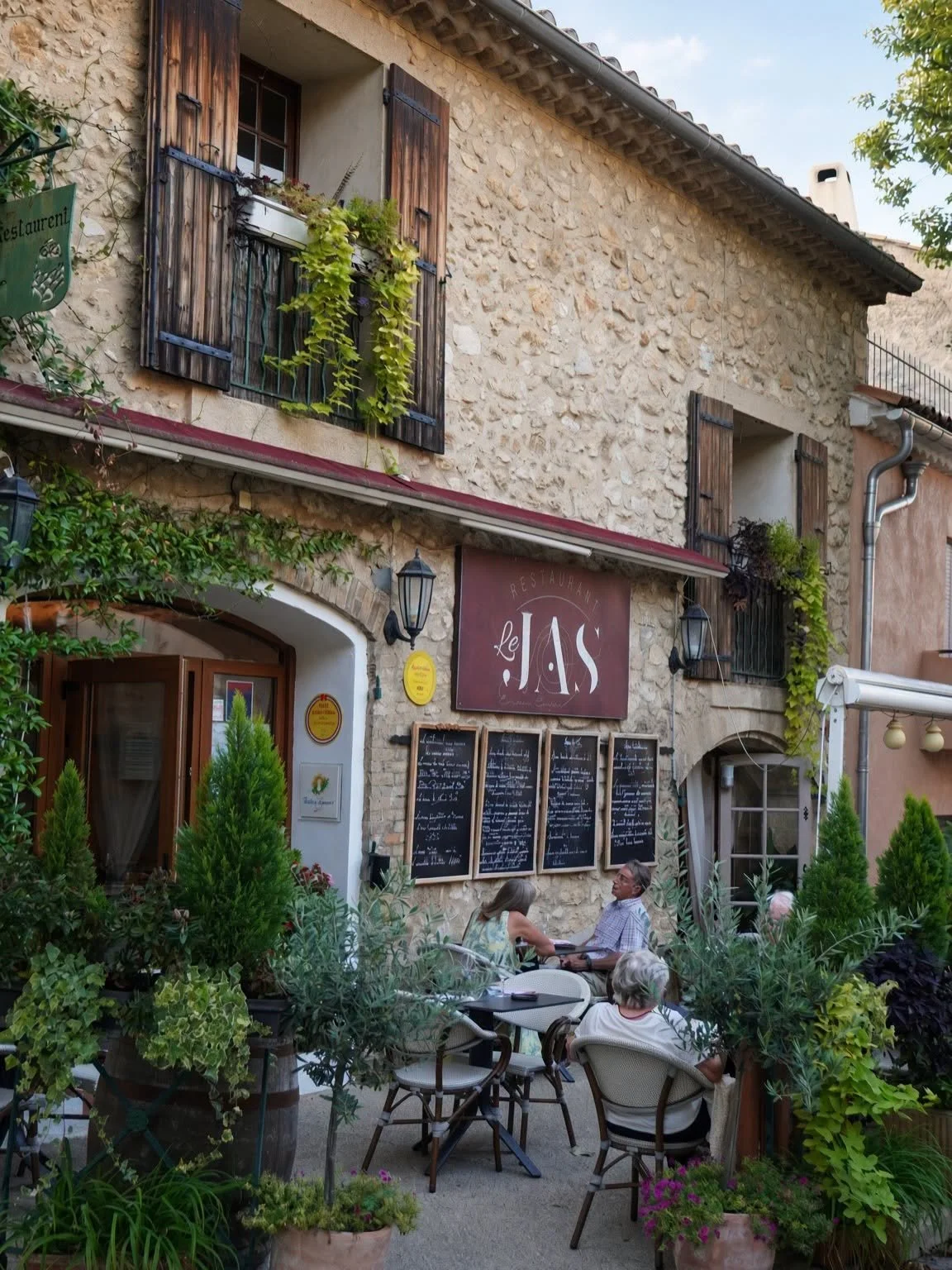 Façade en pierre du restaurant Le Jas et sa terrasse fleurie au cœur de La Roque-d'Anthéron
