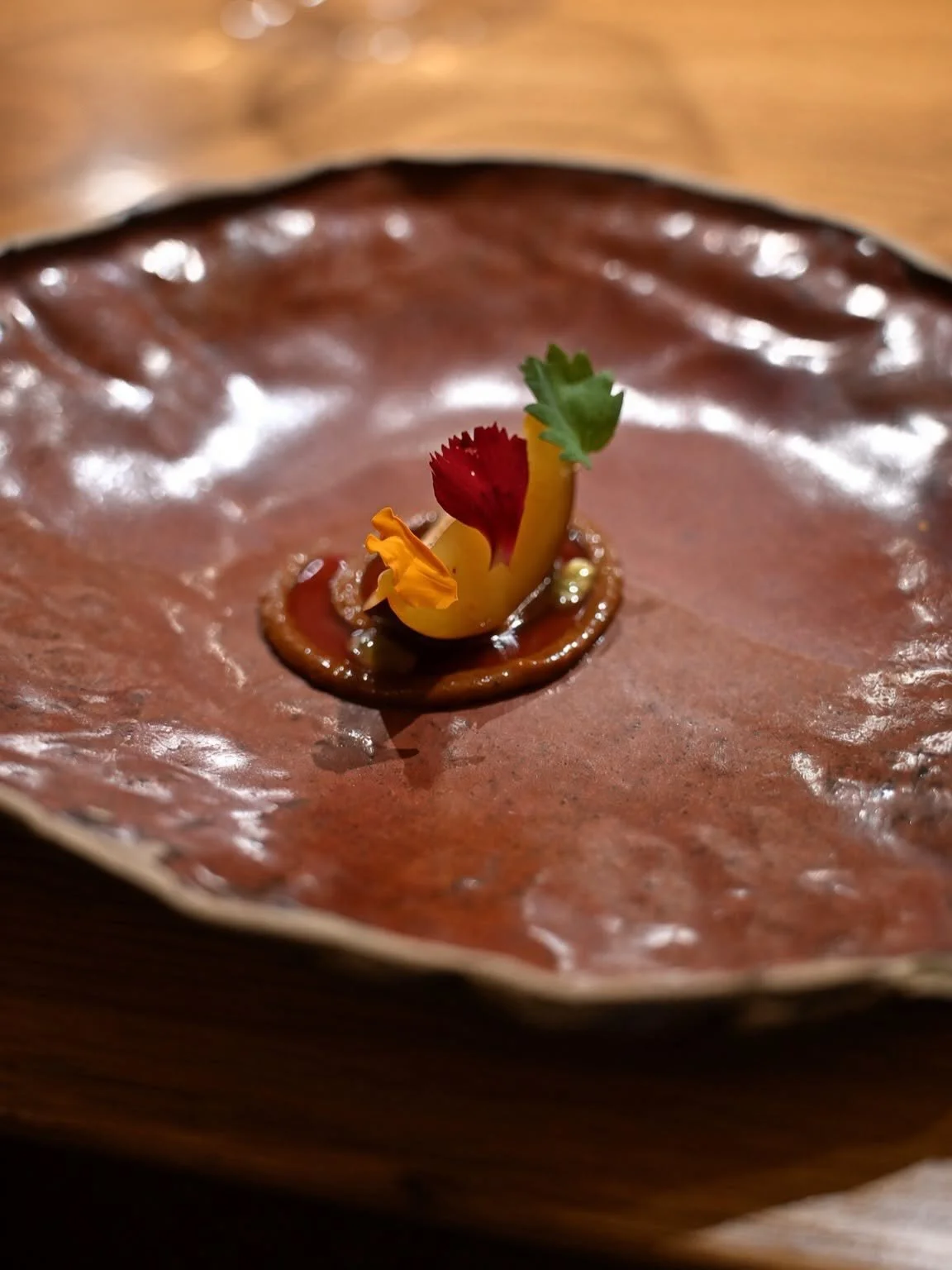 Petite bouchée colorée posée au centre d'une grande assiette en céramique brun cuivré