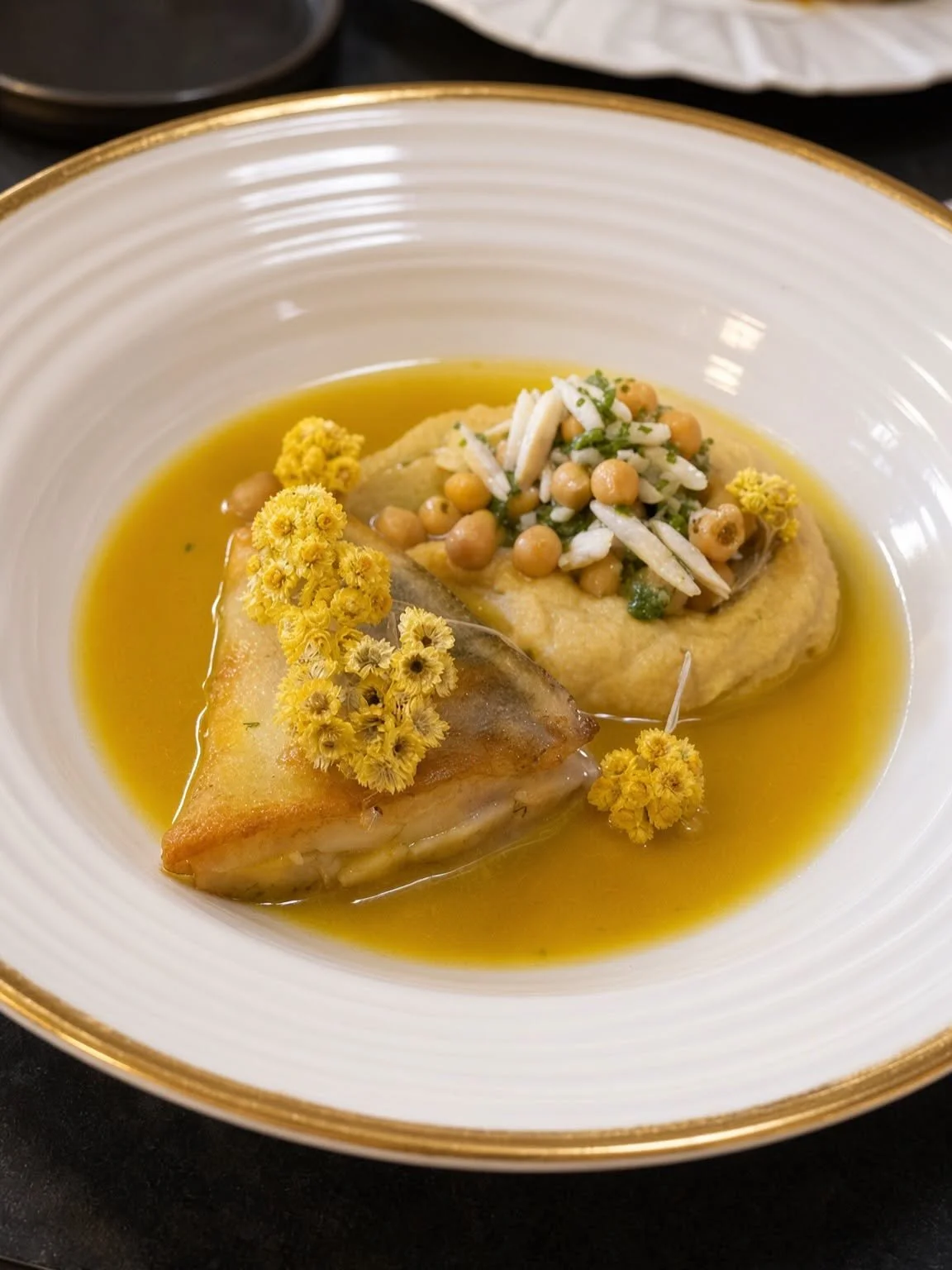 Assiette du chef nappée d'une sauce dorée et décorée de petites fleurs