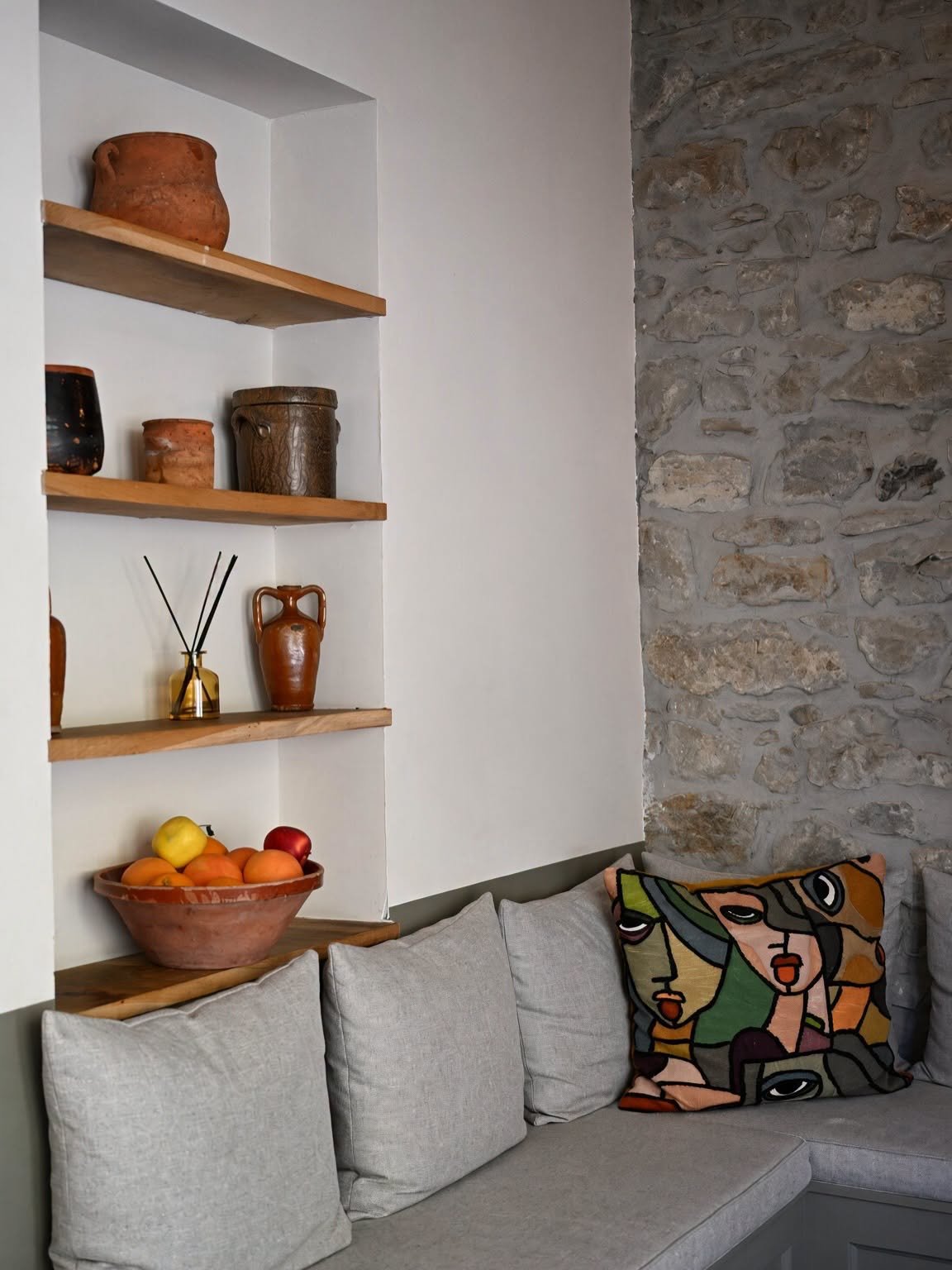 Coin salon avec banquette, coussins colorés et niches décorées de poteries