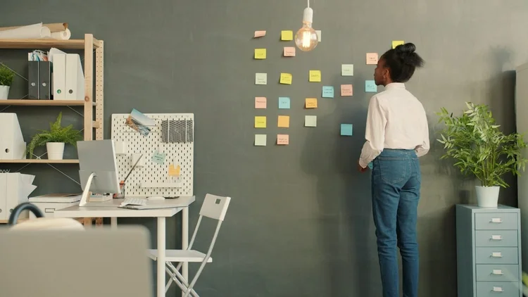 Une personne, vue de dos, colle des notes adhésives sur un mur lors d’un atelier de travail