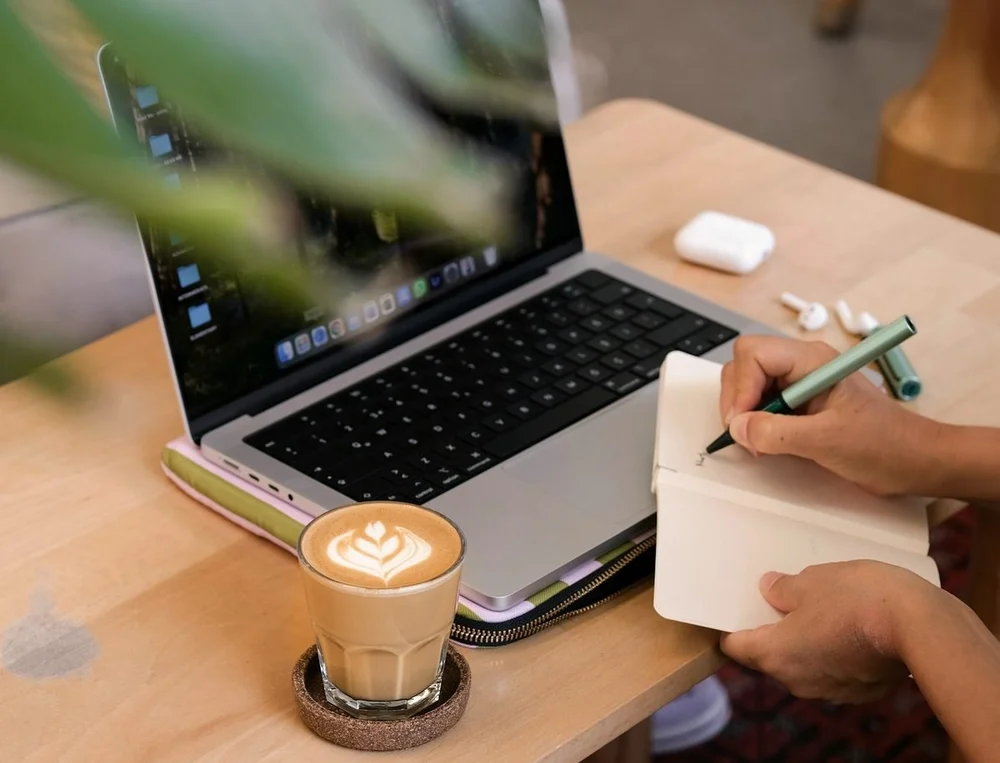 Ordinateur portable, carnet et café sur une table : une personne prend des notes