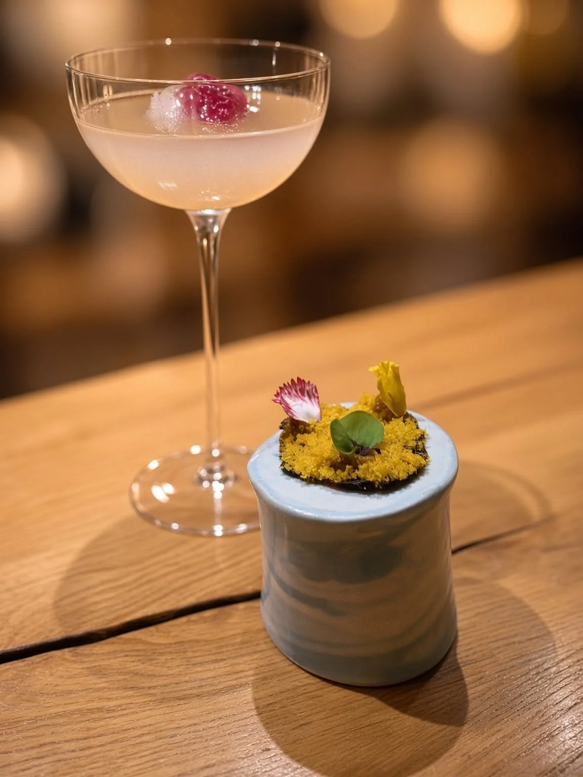 Cocktail servi dans un verre à pied à côté d'une première bouchée colorée posée sur un socle en céramique