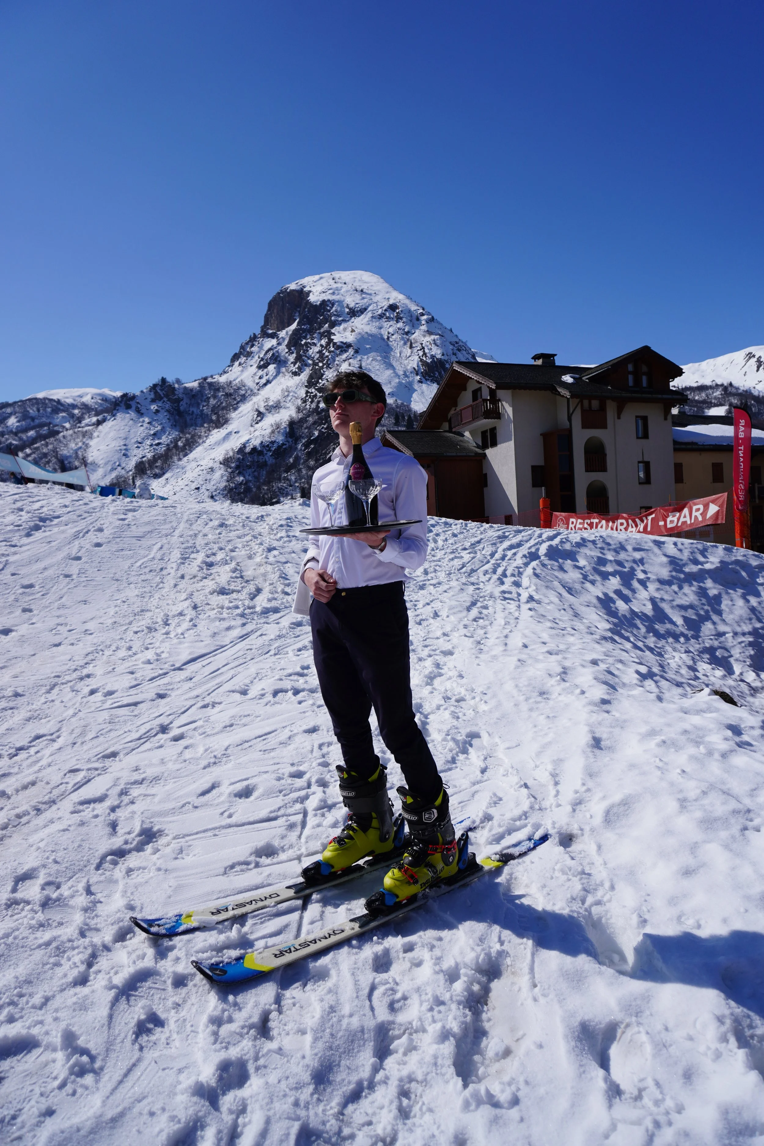 Trois personnes posant pour une vidéo ou une photo devant un mur en brique, avec un téléphone en première plan enregistrant leur image, où elles tiennent plusieurs objets de différentes couleurs.