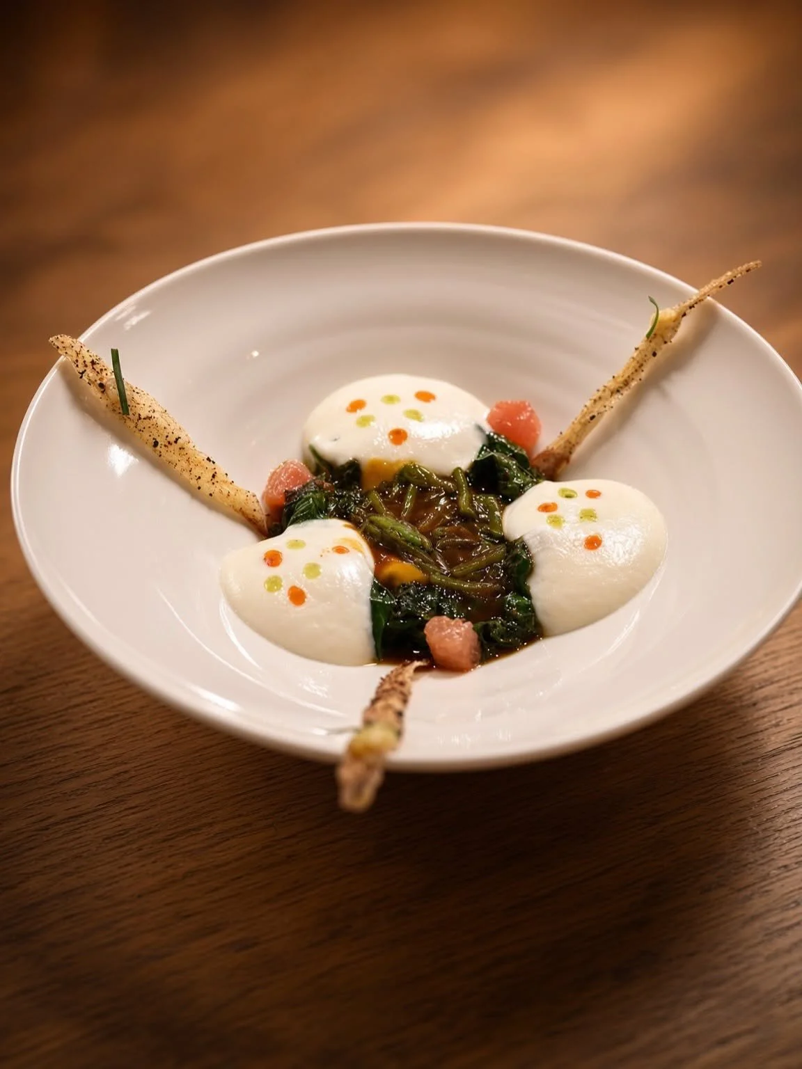 Assiette blanche creuse dressée avec précision, des touches blanches et vertes et deux tuiles dorées