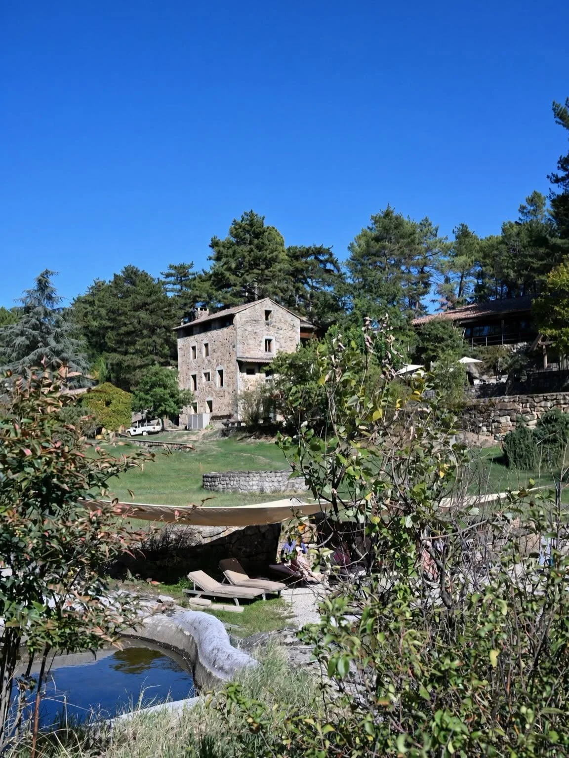 Bâtisse en pierre du Domaine du Taillé entourée de verdure, au-dessus de la piscine naturelle