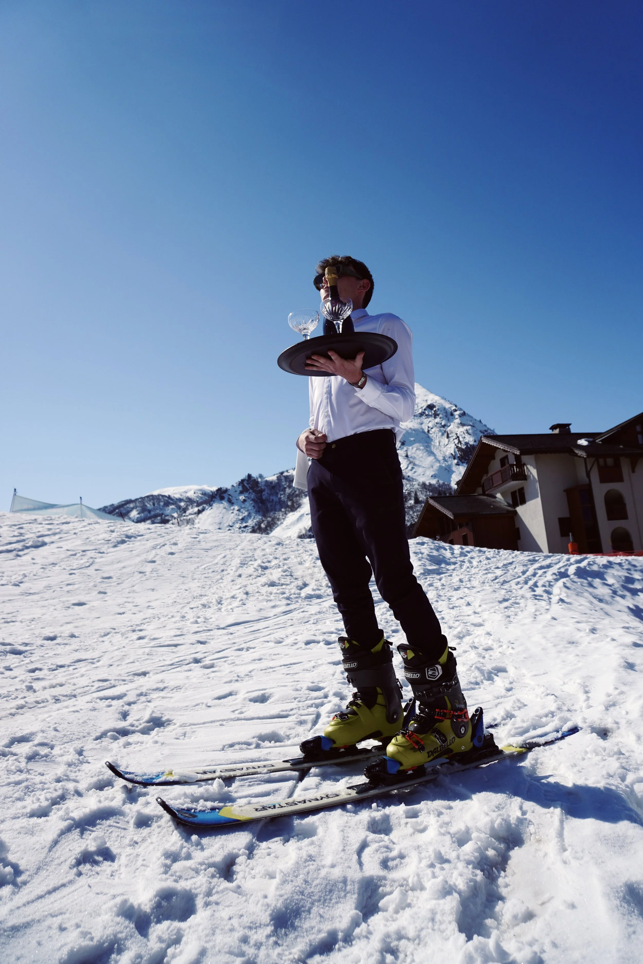 Trois personnes posant pour une vidéo ou une photo devant un mur en brique, avec un téléphone en première plan enregistrant leur image, où elles tiennent plusieurs objets de différentes couleurs.