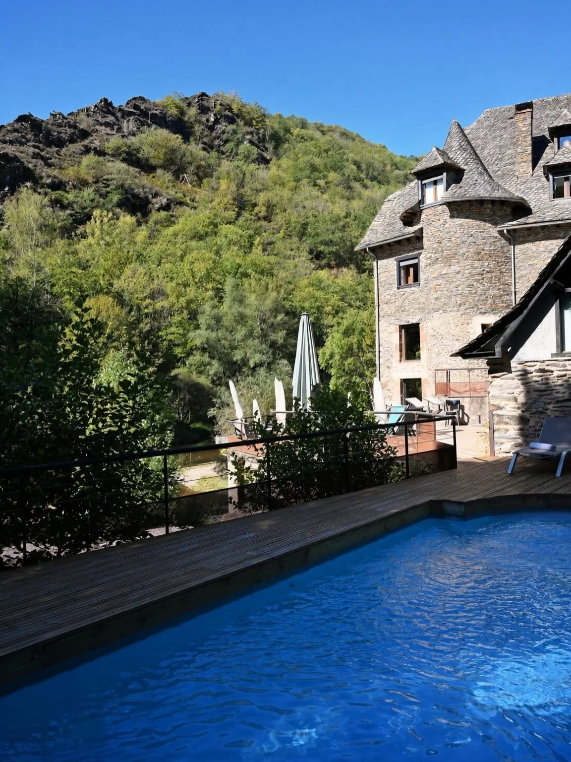 Piscine du Moulin de Cambelong face aux collines boisées et à la bâtisse en pierre