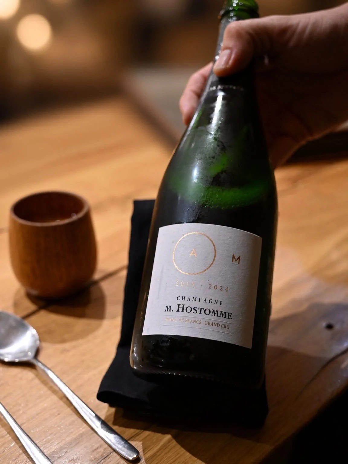 Bouteille de champagne M. Hostomme présentée à table, enveloppée dans une serviette noire