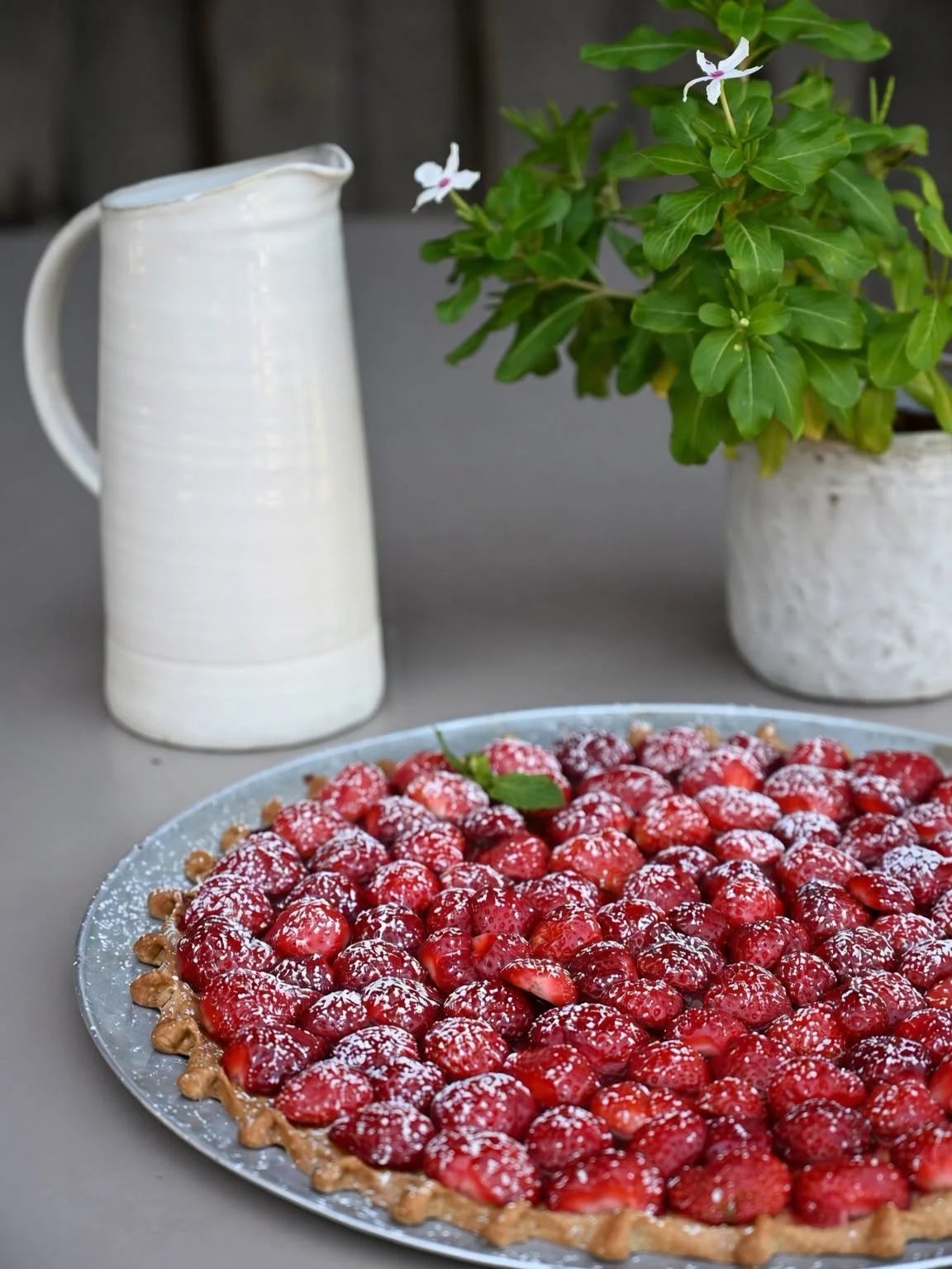 Tarte aux framboises fraîches à côté d'une carafe blanche et d'un pot de basilic