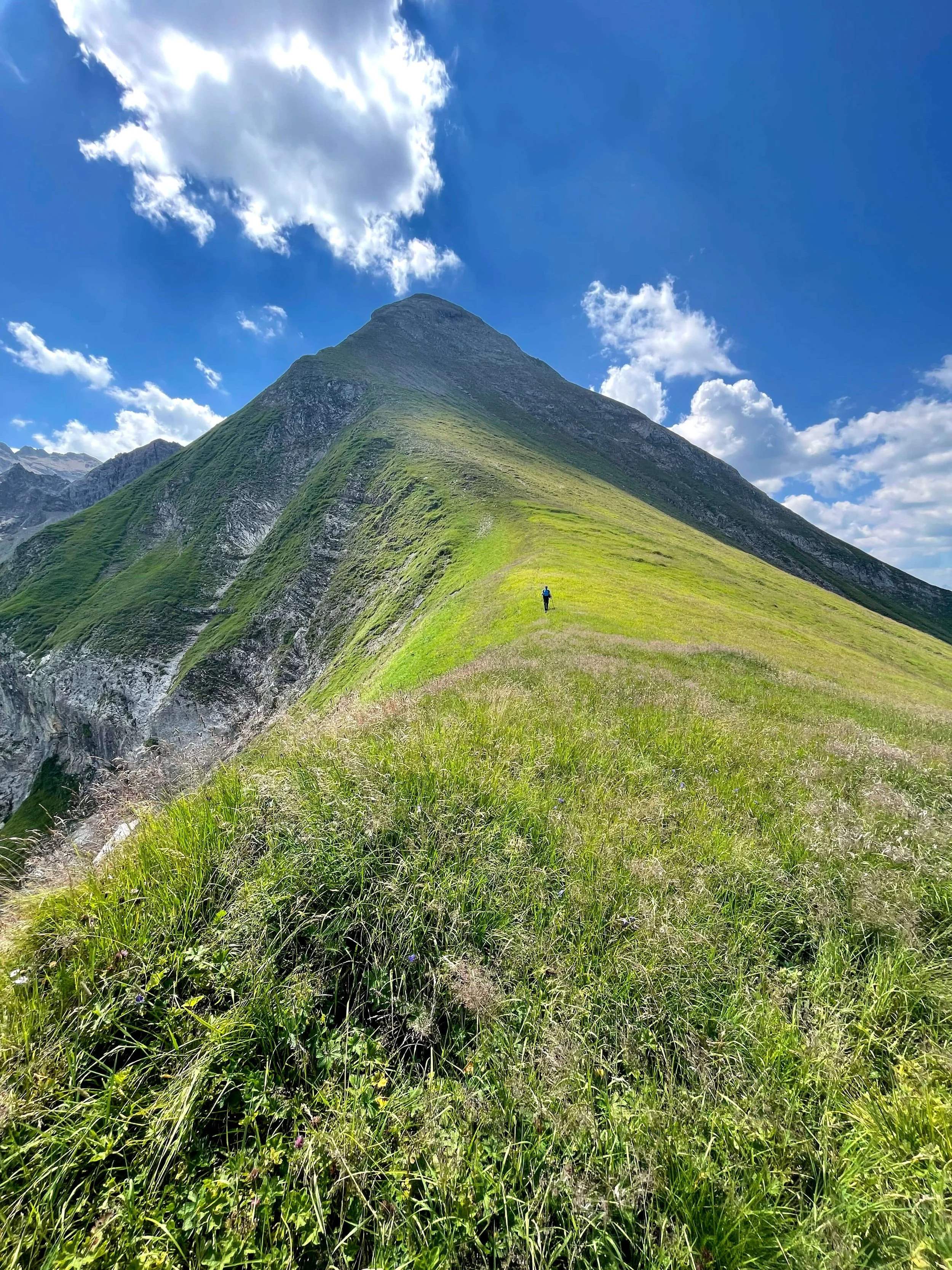Wandernde Person auf einem grünen Berggrat auf dem Weg zum Gipfel