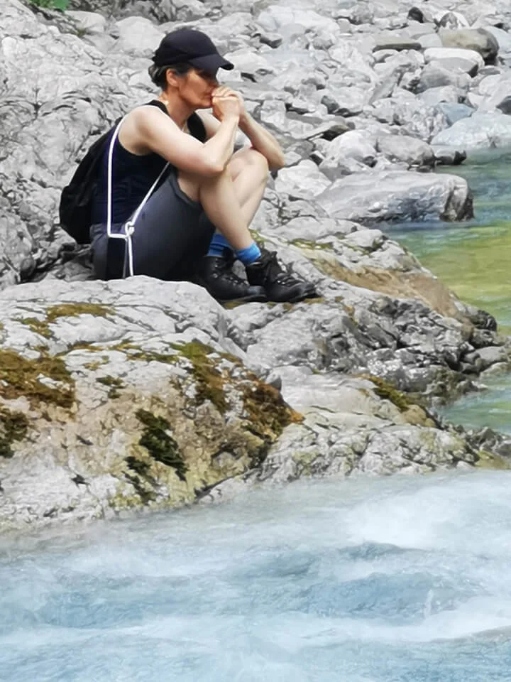 Person sitzt nachdenklich auf einem Felsen am Fluss