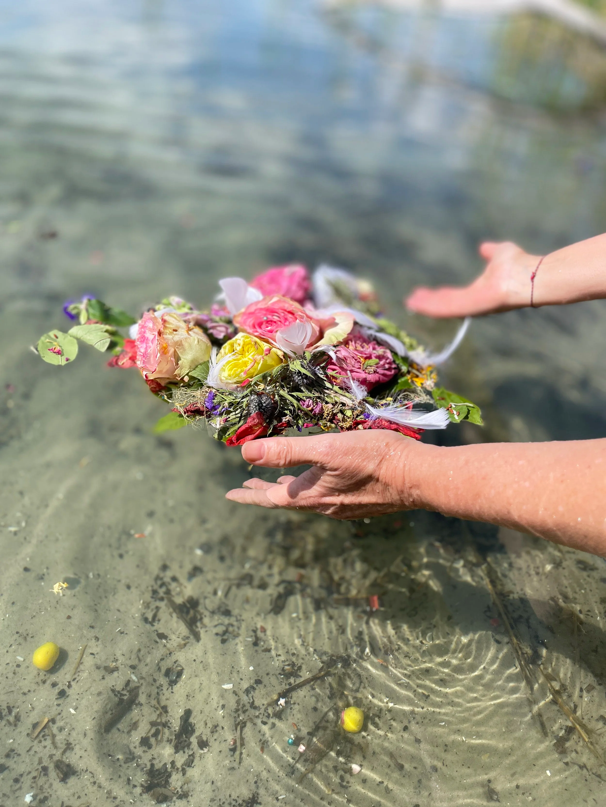 Symbolbild einer Übergabe: Eine rituelle Gabe schwebt auf klarem Seewasser, sanft geführt von den Händen der Zeremoniemeisterin Birgit Gentis