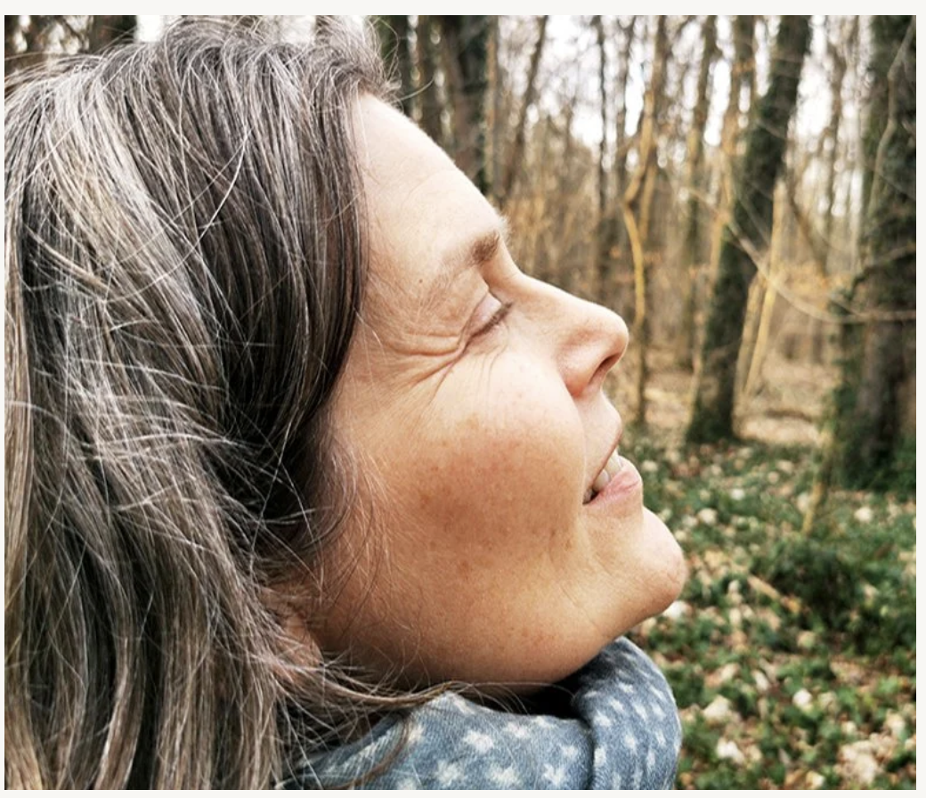 Birgit Gentis im Profil mit geschlossenen Augen, das Gesicht im Wald dem Licht zugewandt.