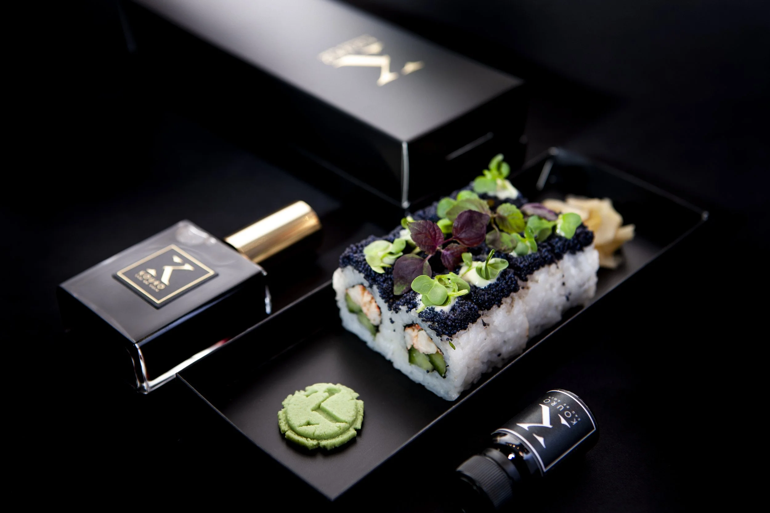 Edle Sushi-Rollen liegen neben einem schwarzen Parfum