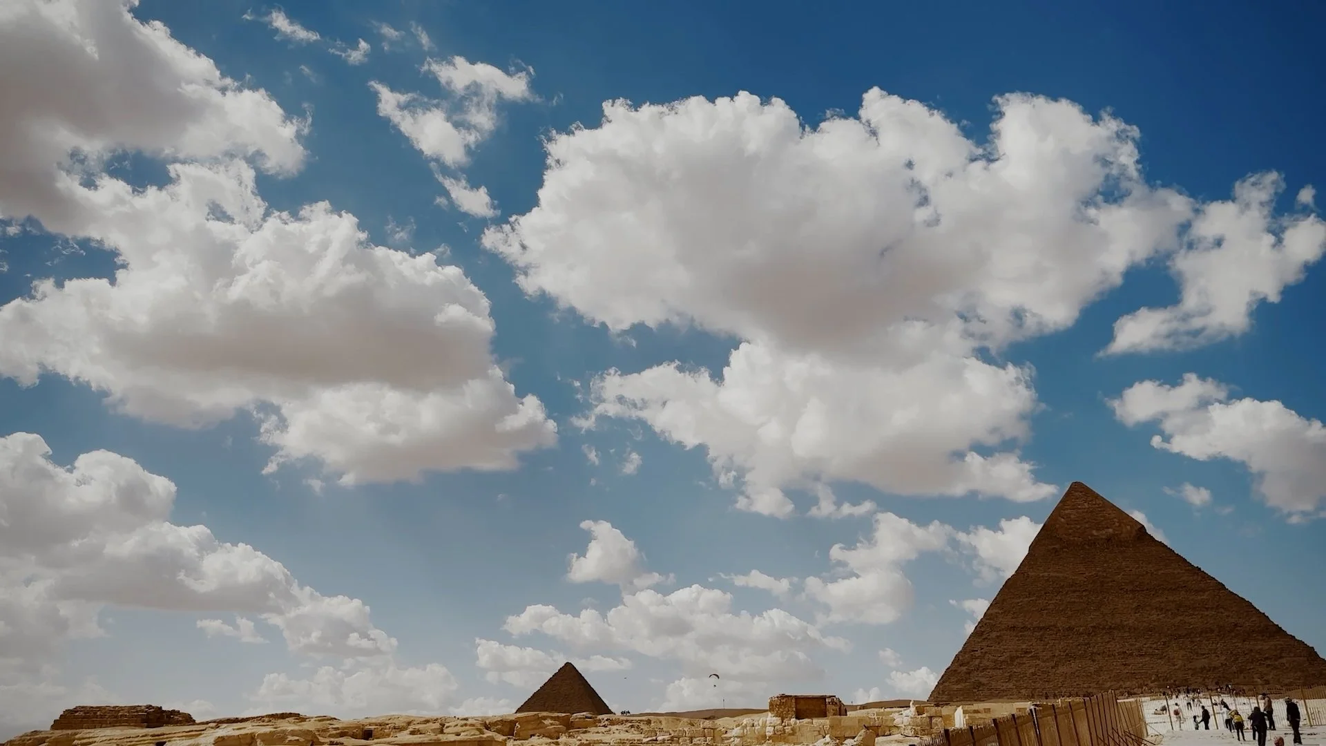 Ancient pyramids in the desert with a blue sky and scattered clouds.