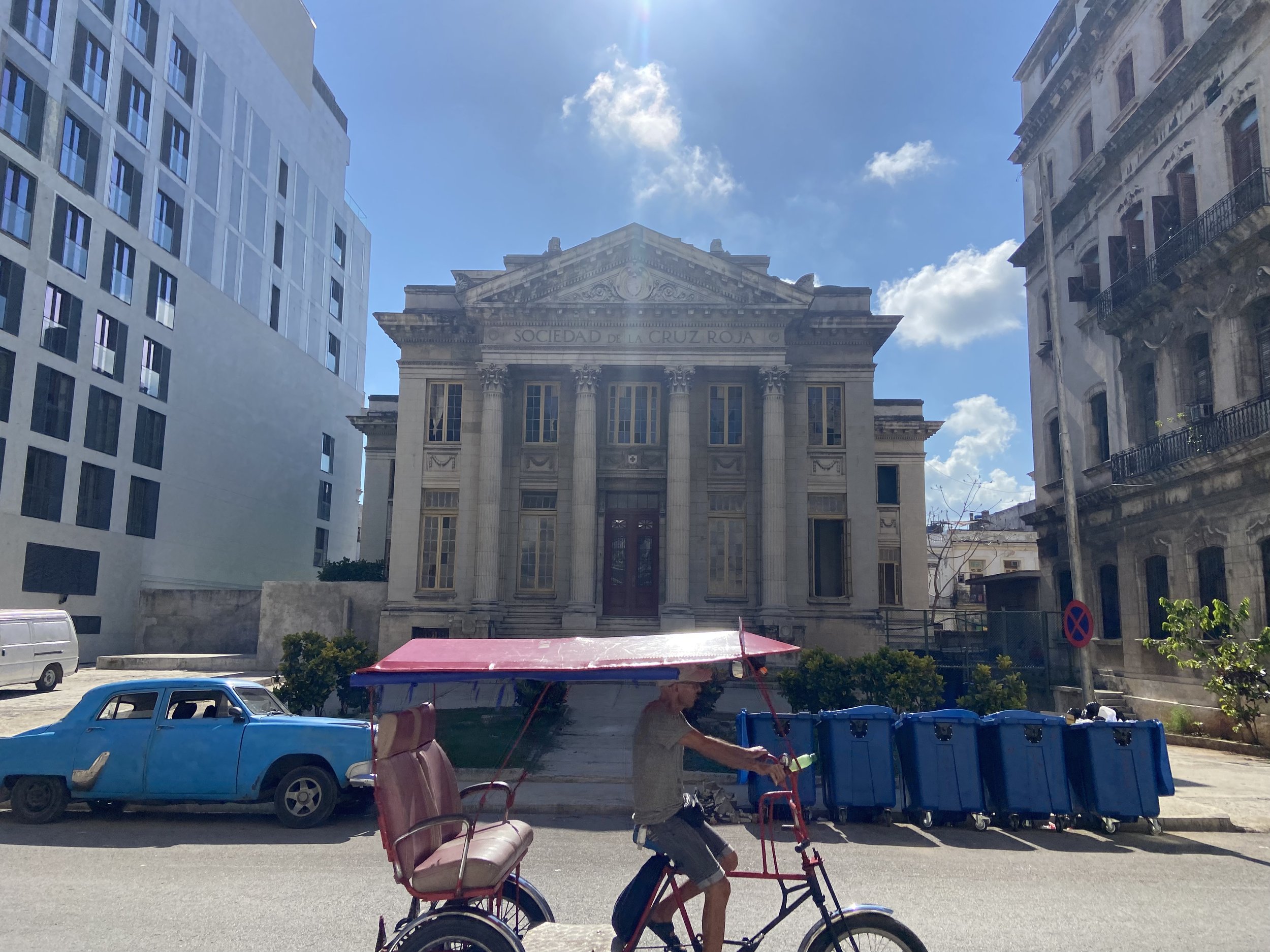 A historic street in Old Havana, a man riding a bicycle taxi, in a beautiful, blue sky day.