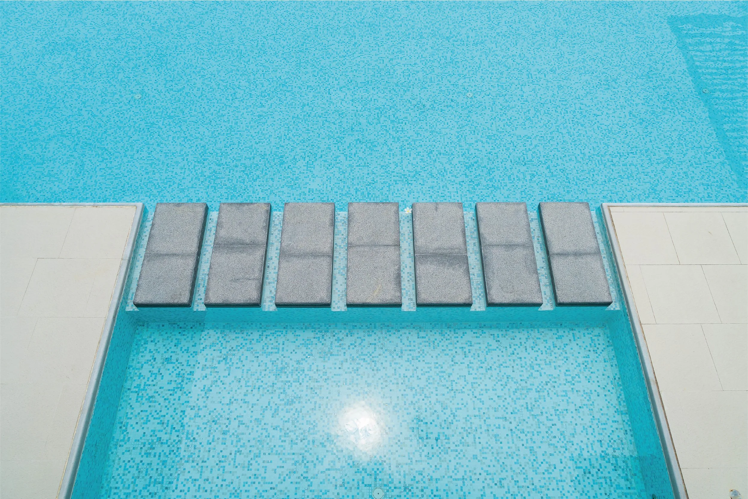 Rectangular stepping stones across a turquoise tiled pool.