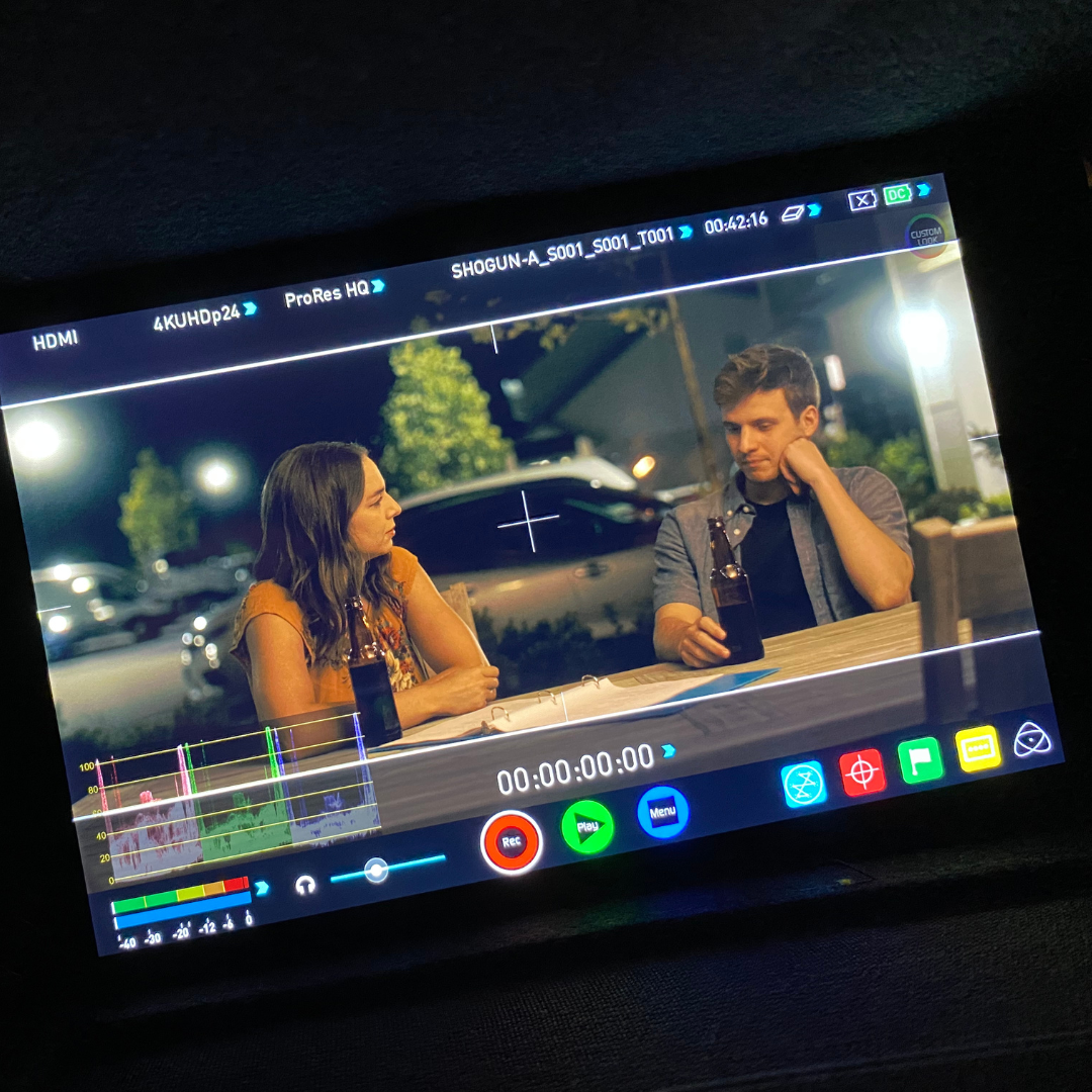 Scene of two people sitting at an outdoor table at night, having drinks and talking, captured on a professional video monitor.