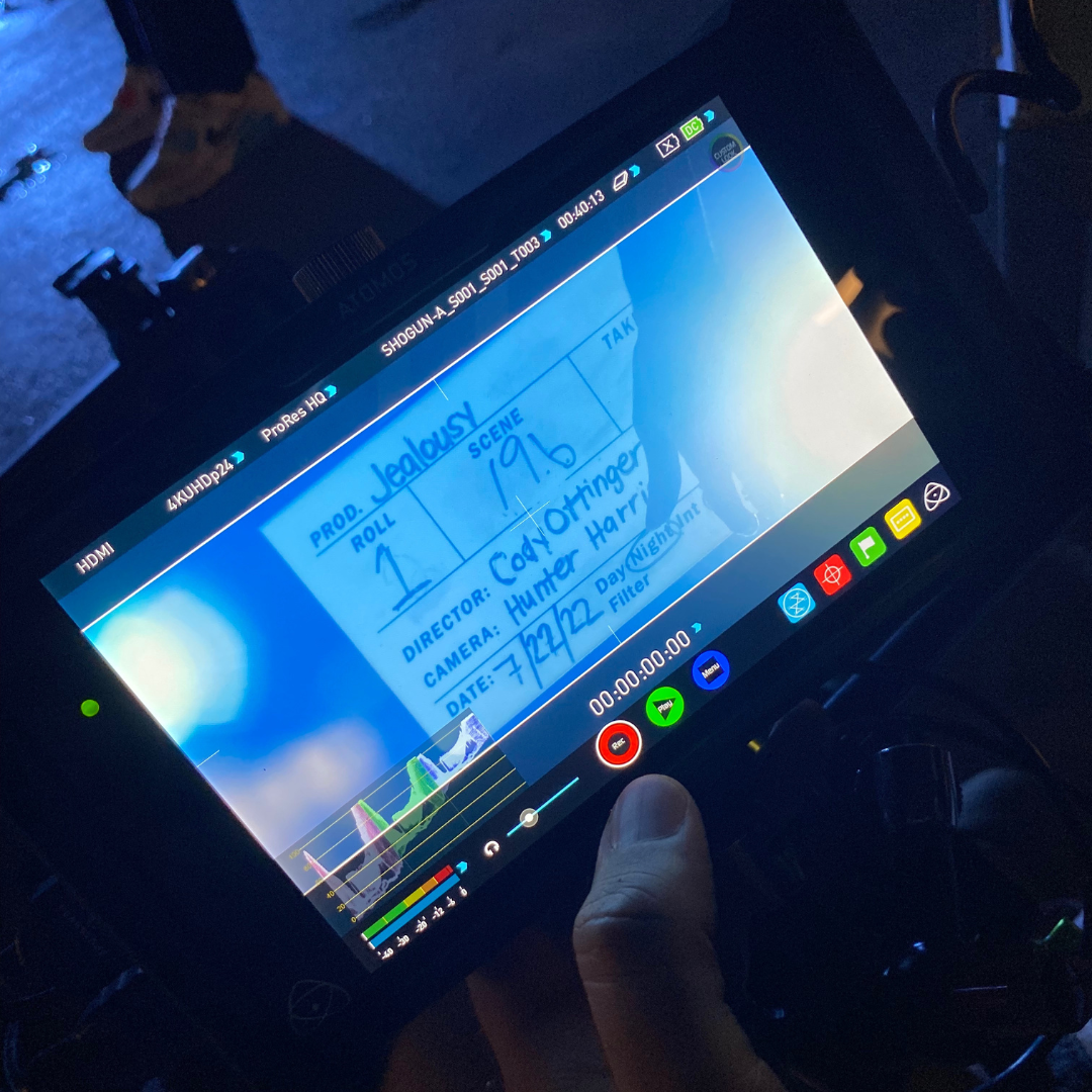 Close-up of a video camera monitor displaying a shot list and scene information for a film project, with text including director, camera, date, and scene details.