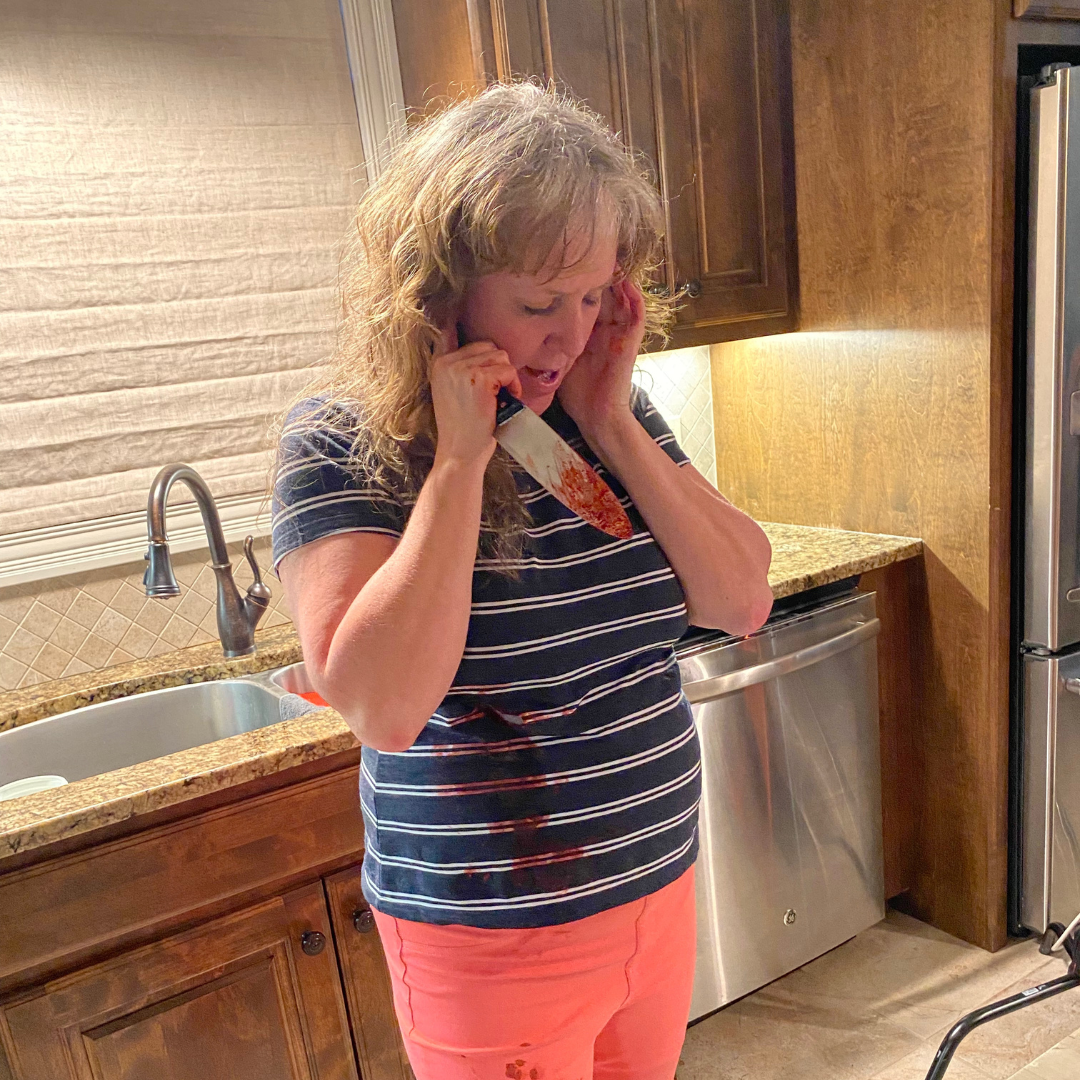 A woman holding a bloody kitchen knife to her neck, appearing distressed, in a home kitchen.