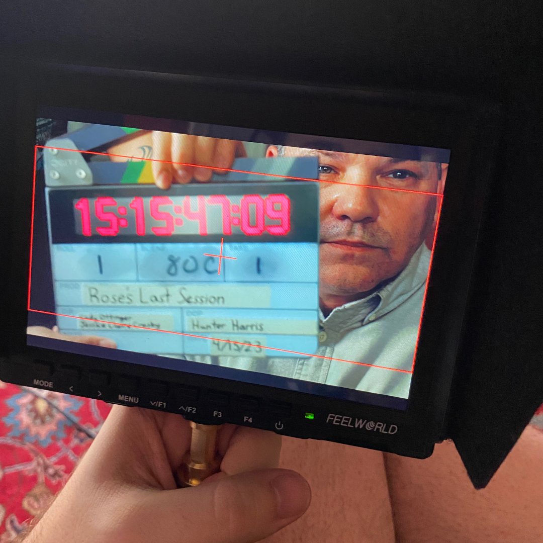 Close-up shot of a man holding a clapperboard with scene details, with another person visible in the background.