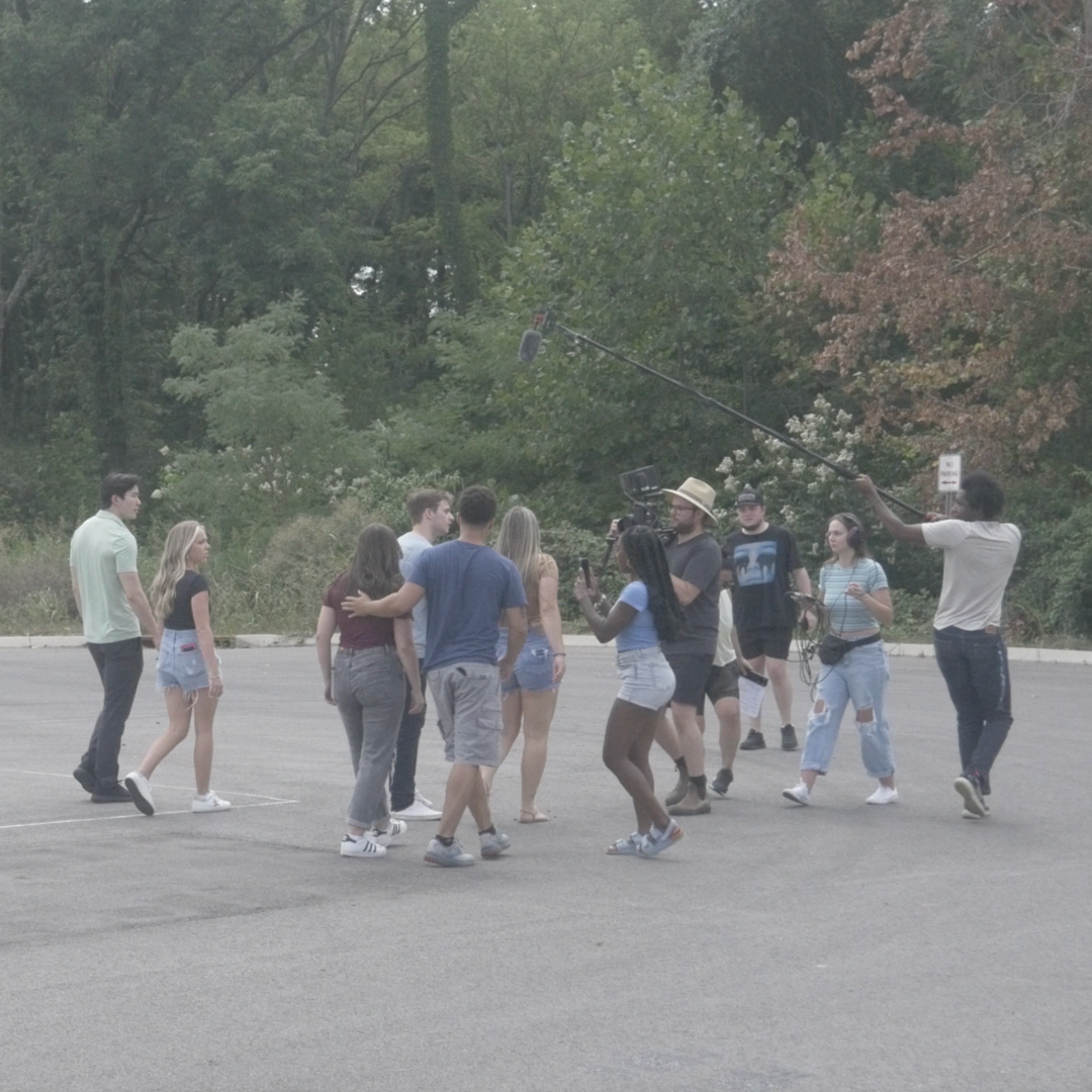 A group of people filming a scene outdoors with trees in the background.