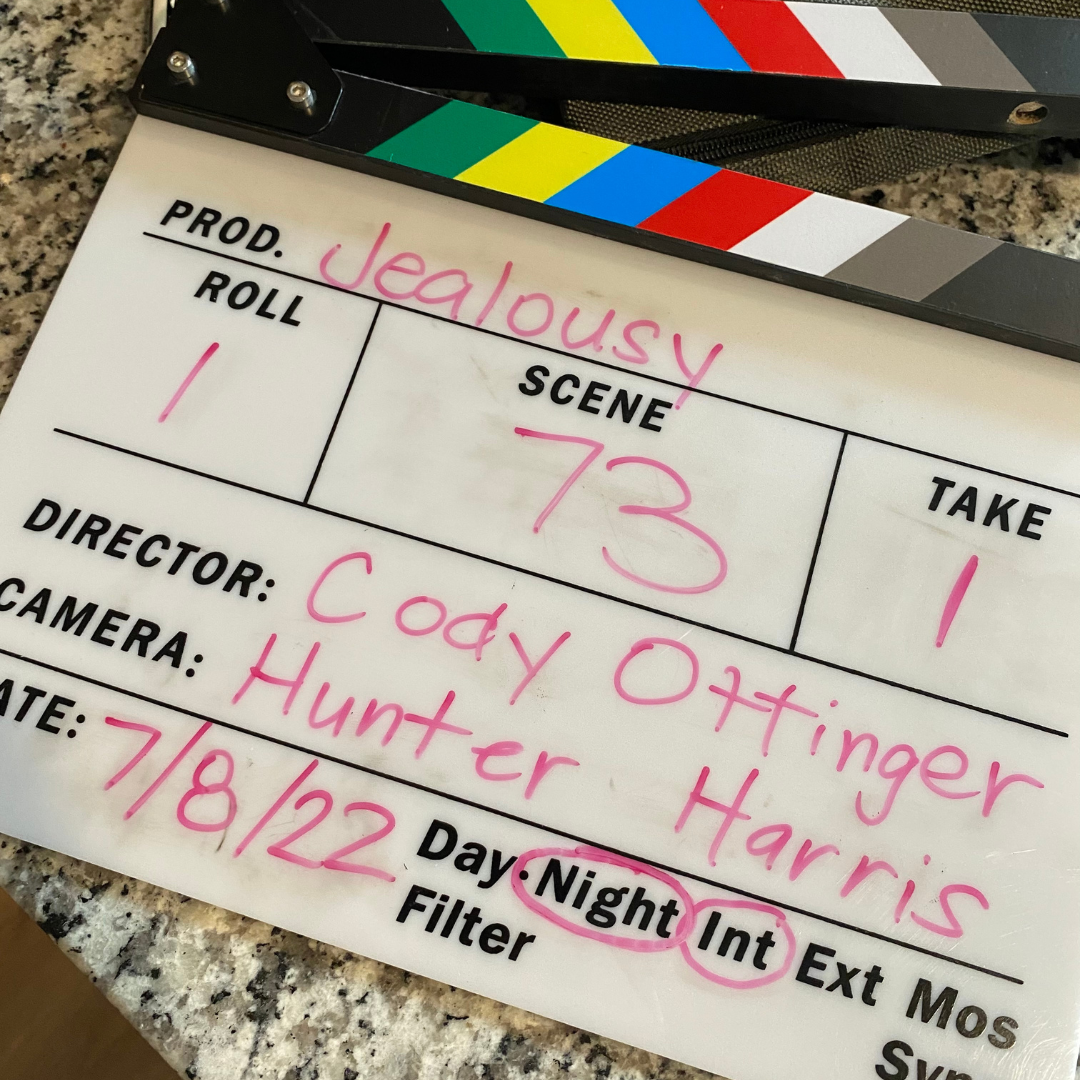 Clapboard slate with handwritten notes for a film or TV scene, including title 'Jealousy', scene 73, and director 'Cody Otlinger'.