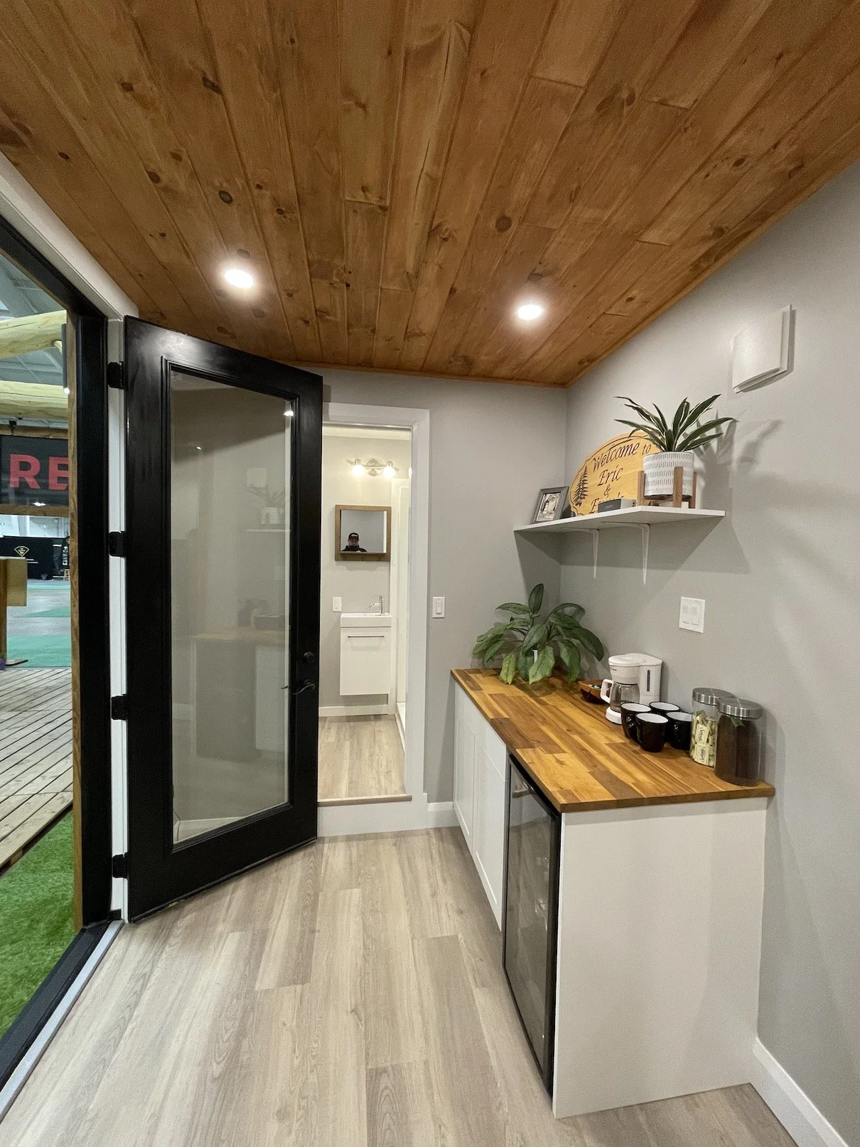 Indoor kitchenette with wooden countertop, mini refrigerator, coffee maker, cups, plants, shelves, and sliding glass door leading outside.