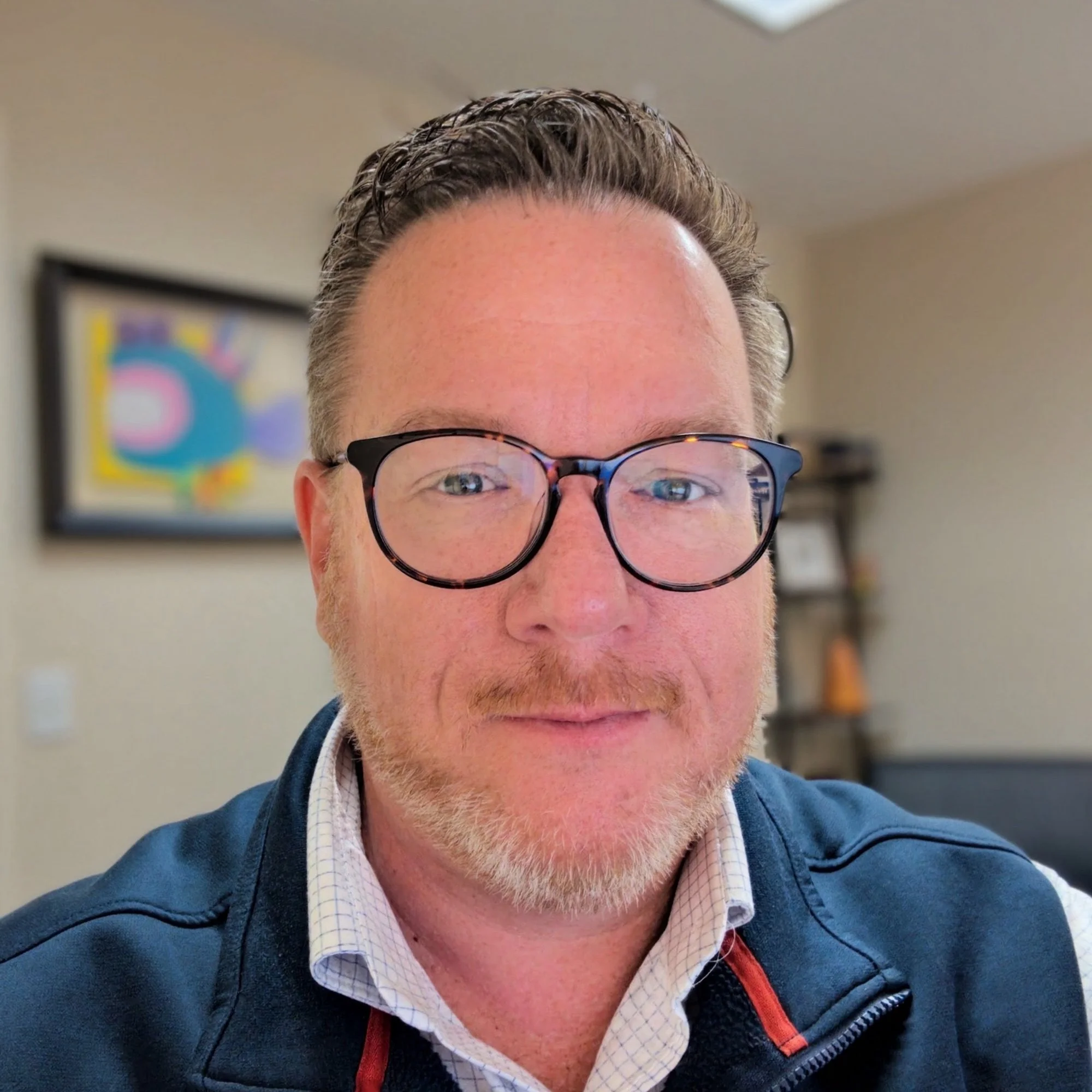 Professional headshot of Eric Berry wearing glasses and a navy jacket, seated indoors with a softly blurred office background.