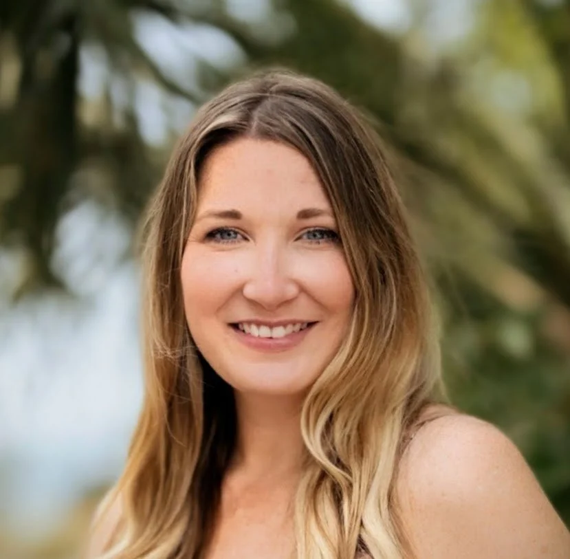 Professional headshot of Cori Wood smiling outdoors, with soft natural light and blurred palm greenery in the background.
