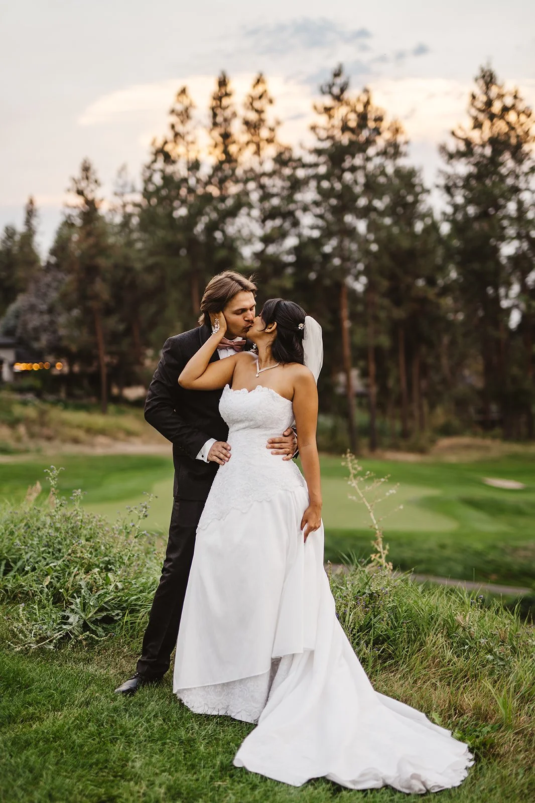 A bride in a wedding dress looking out a window, touching her face with her hand, with a veil and hair accessories.