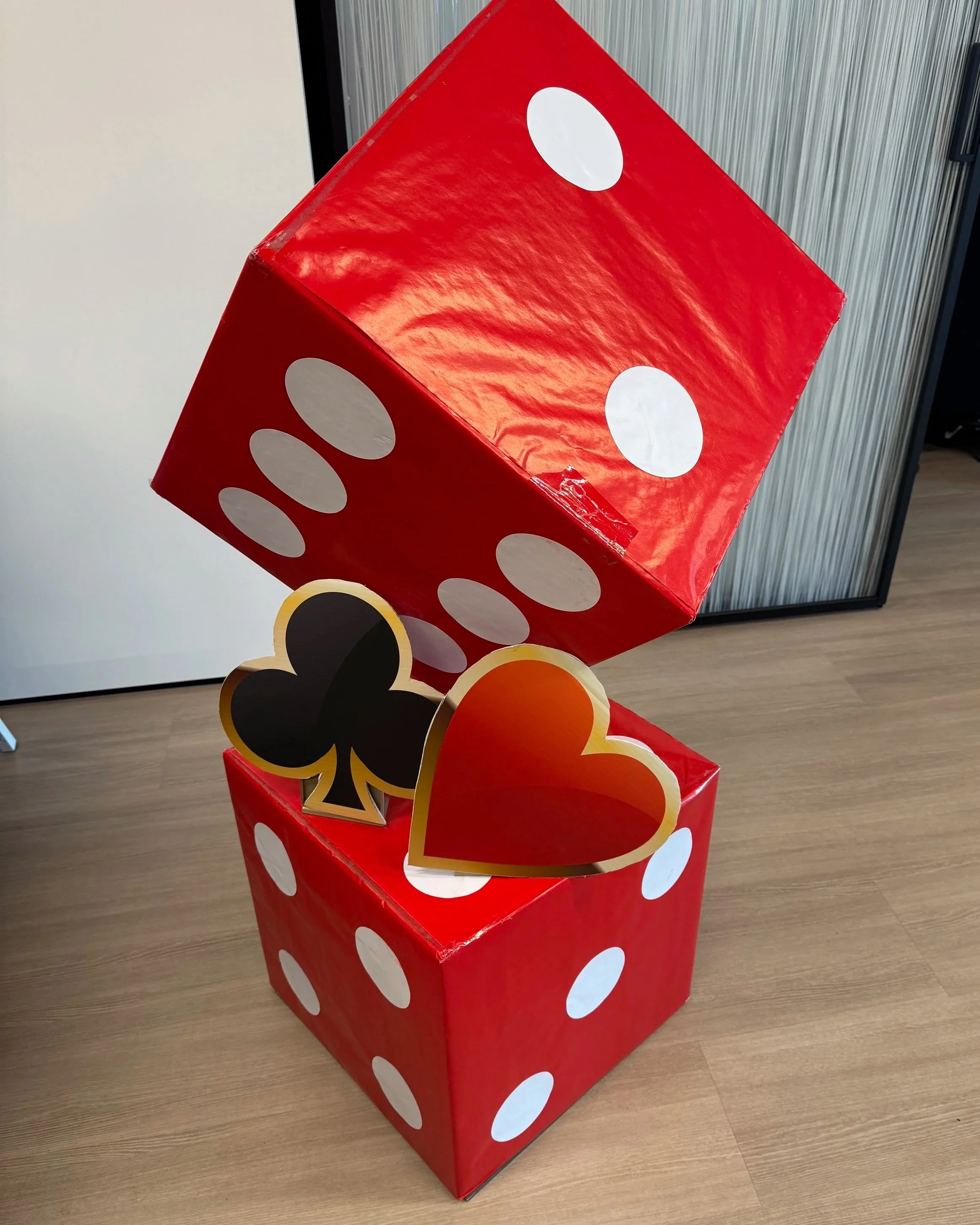 Vineyard with lush green grapevines in foreground, a residential area with trees and houses in the middle ground, and a large body of water with mountains in the background under a sunset sky.