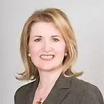 A woman with shoulder-length blonde hair, wearing a gray blazer and a light-colored top, smiling at the camera.