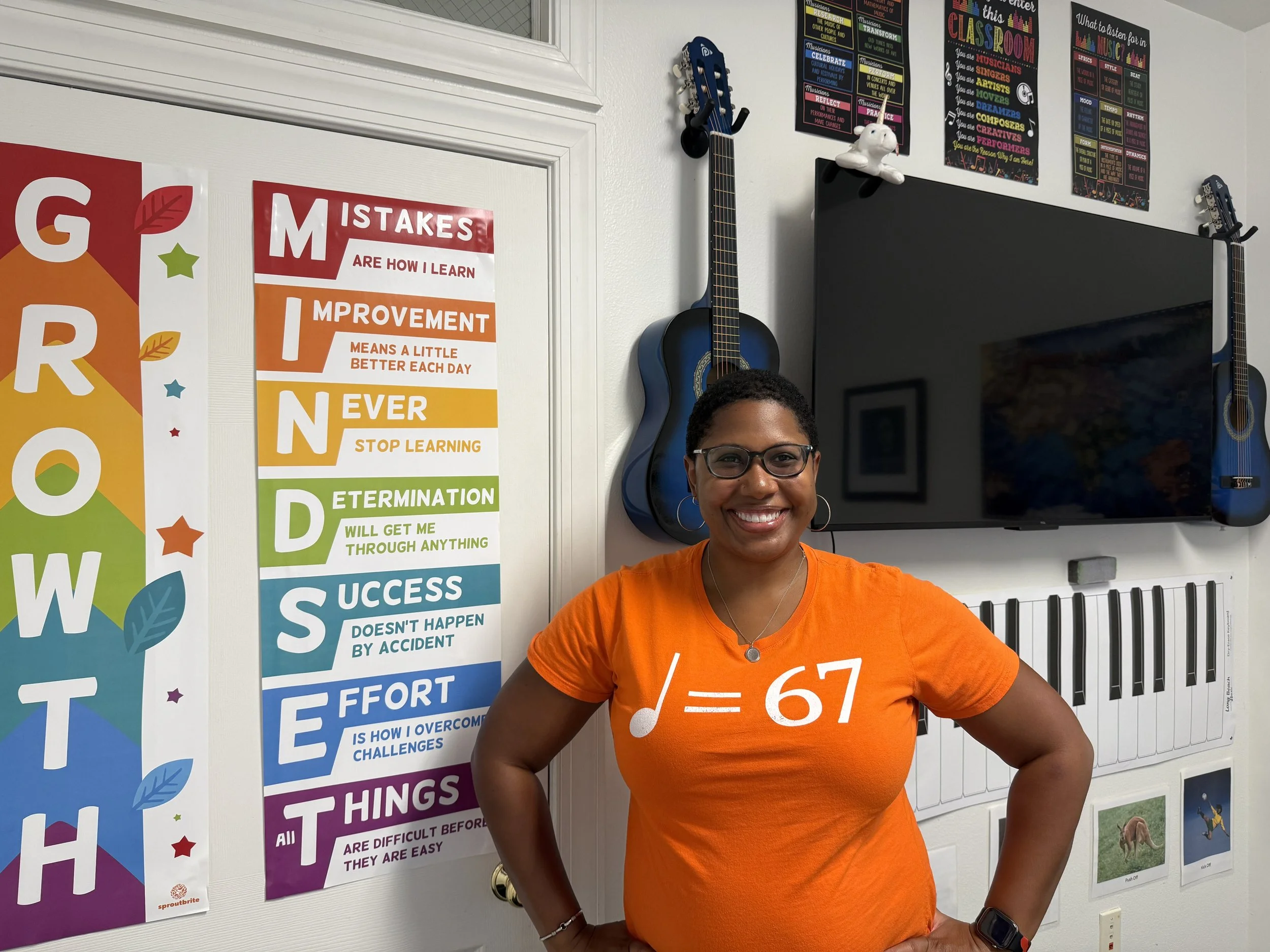 Piano teacher standing in front of motivational poster, guitars, and display.