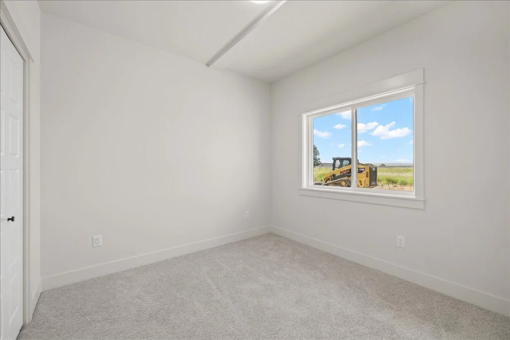 Empty white room with beige carpet, window showing a tractor outside, and closed door.