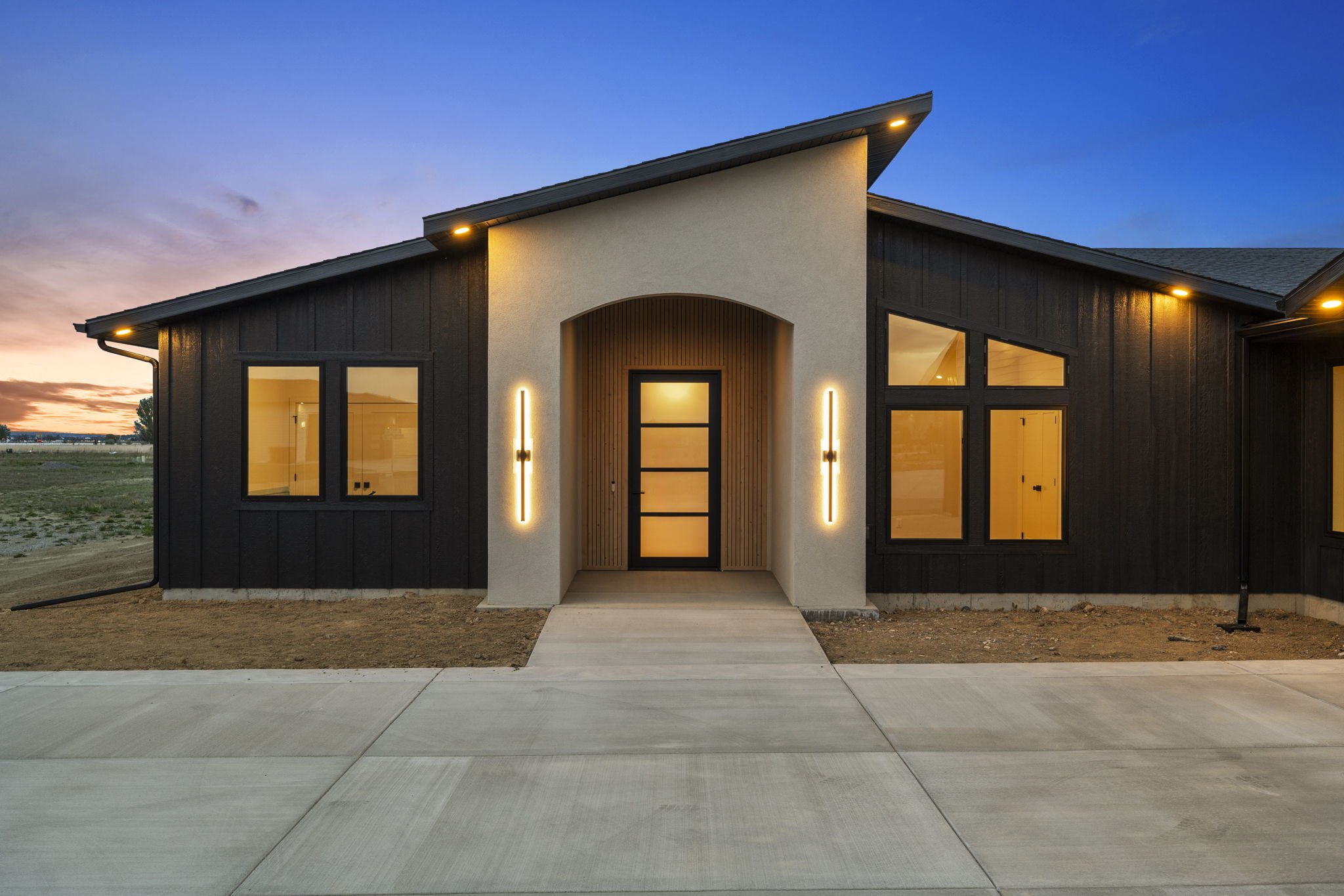 Modern house with black and white exterior, illuminated entrance, and large windows at dusk.