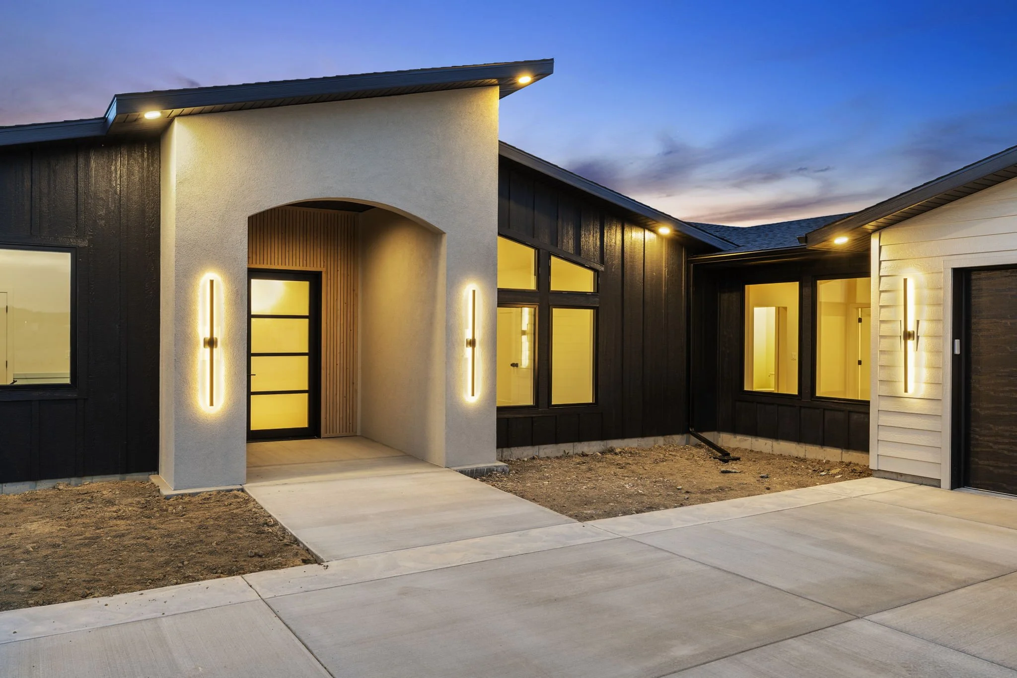 Modern house with black and white exterior, large windows, and outdoor lighting during dusk.